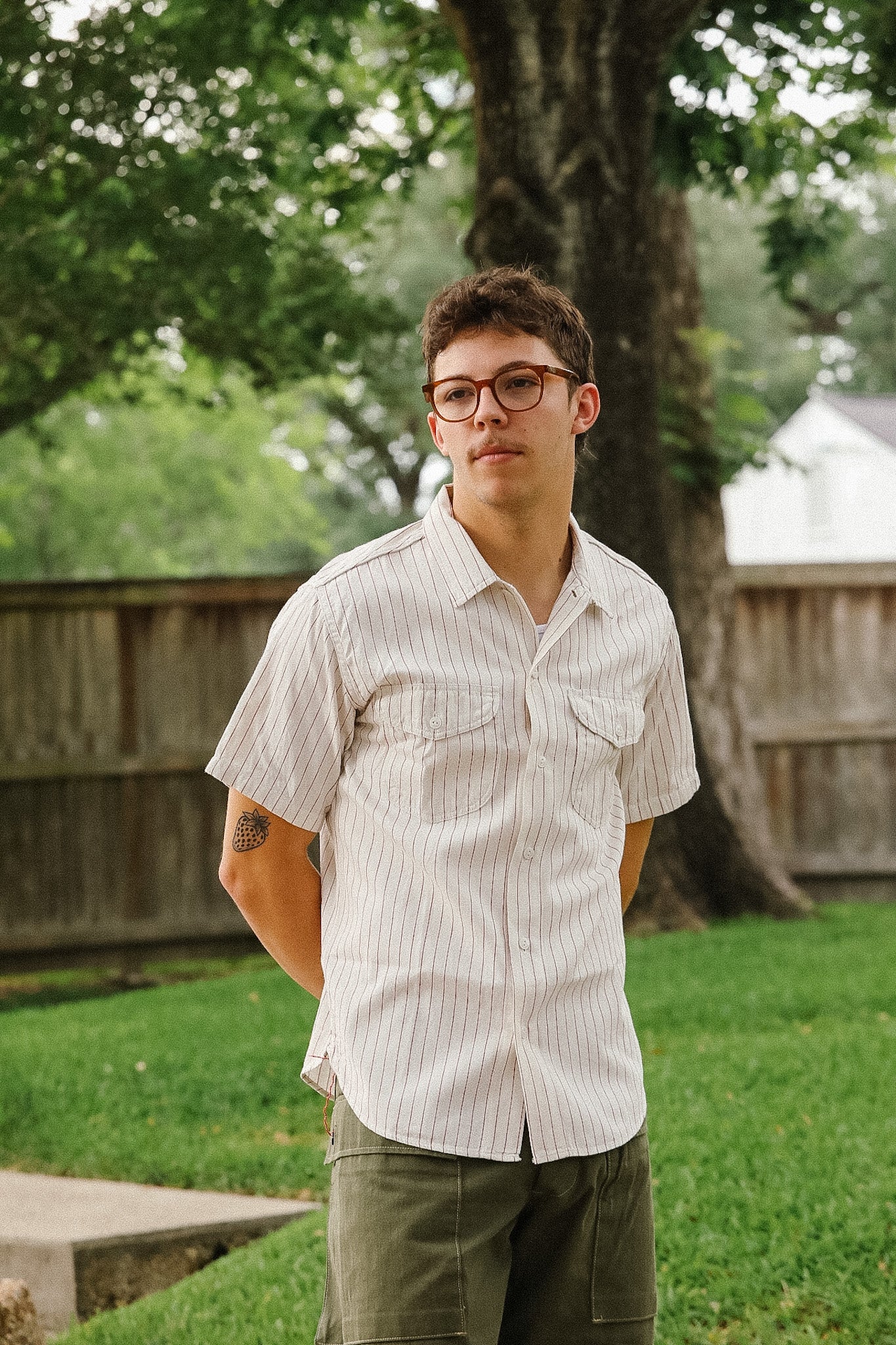 Man wearing glasses and a light shirt standing outdoors with trees and grass in the background