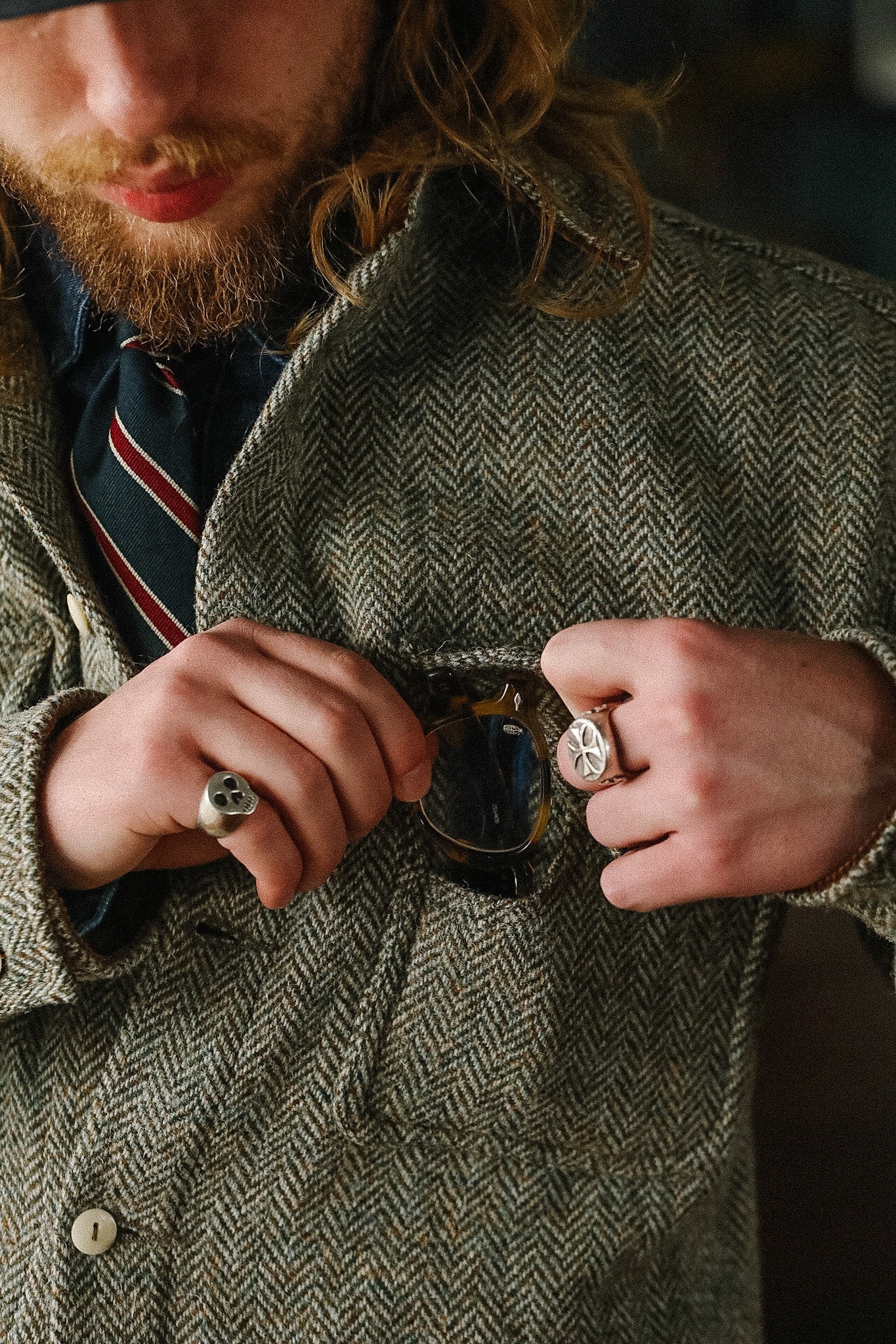 Man in a tweed jacket buttoning his coat with sunglasses in his pocket.