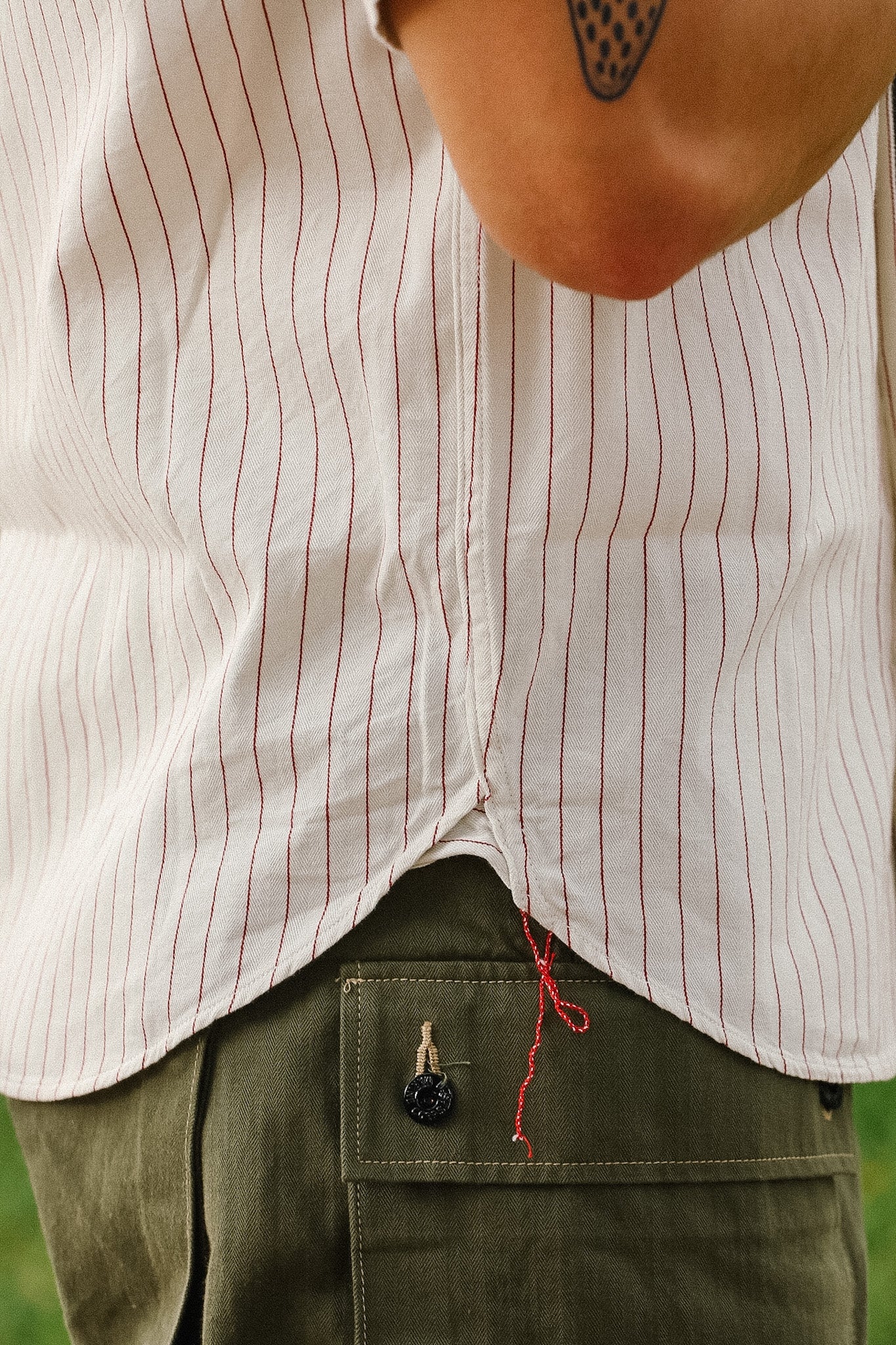 Person wearing a white shirt with red stripes and green pants in an outdoor setting