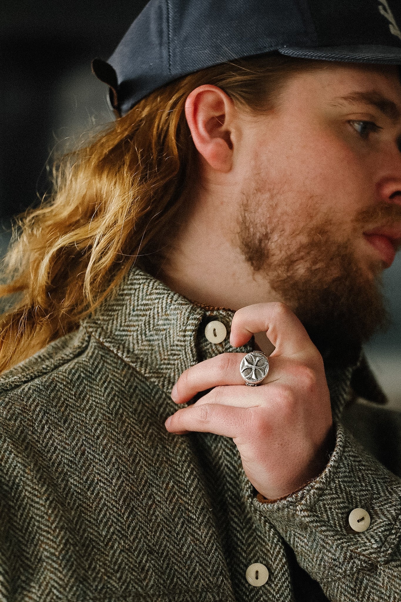 Man with long hair wearing a cap and coat, holding a ring.