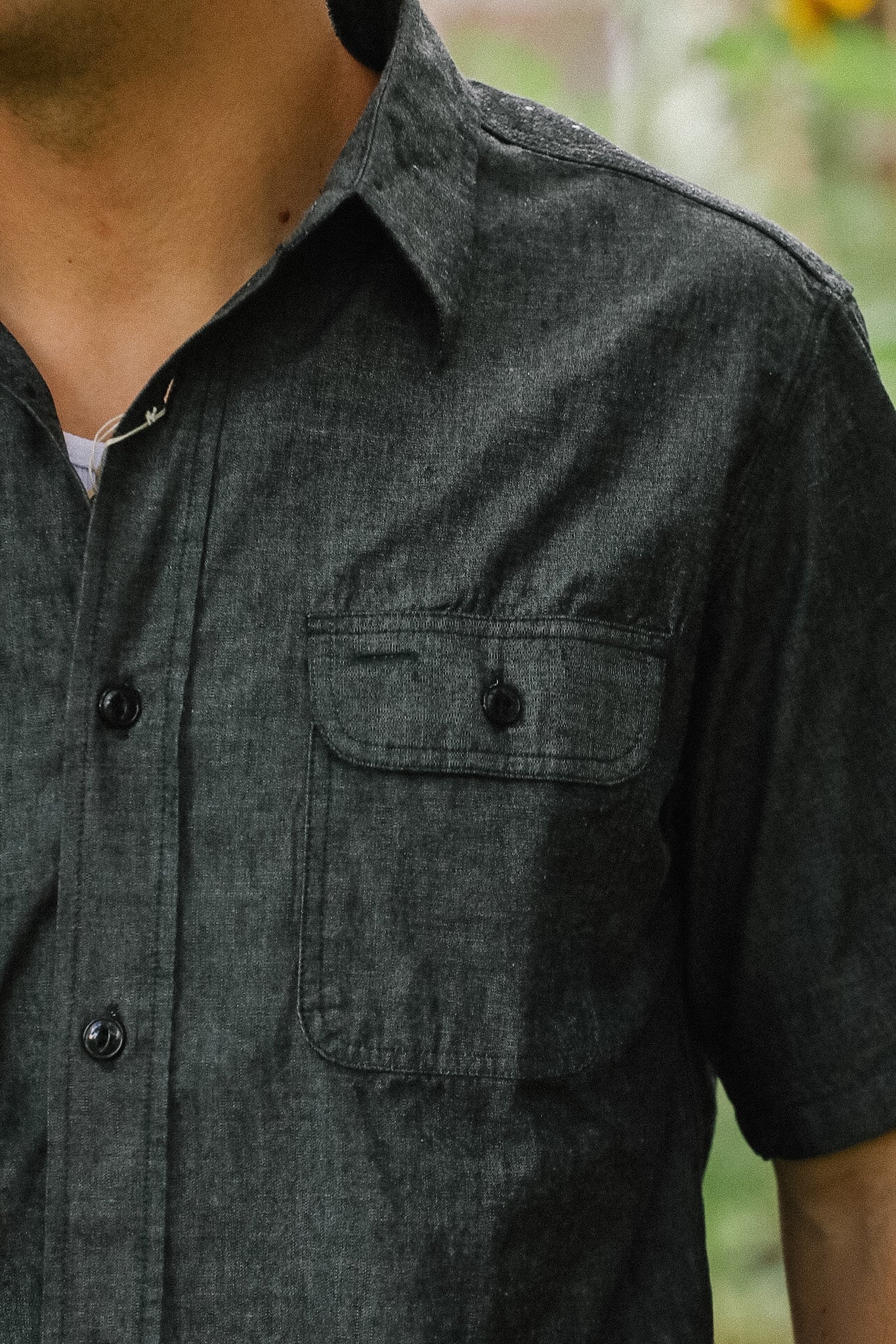 Close-up of a person wearing a dark gray short-sleeve shirt with a blurred background