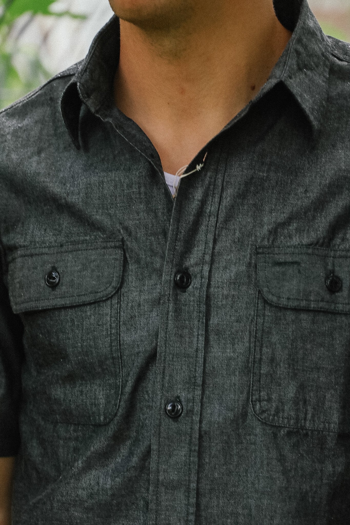 Close-up of a person wearing a dark gray button-up shirt with two front pockets.