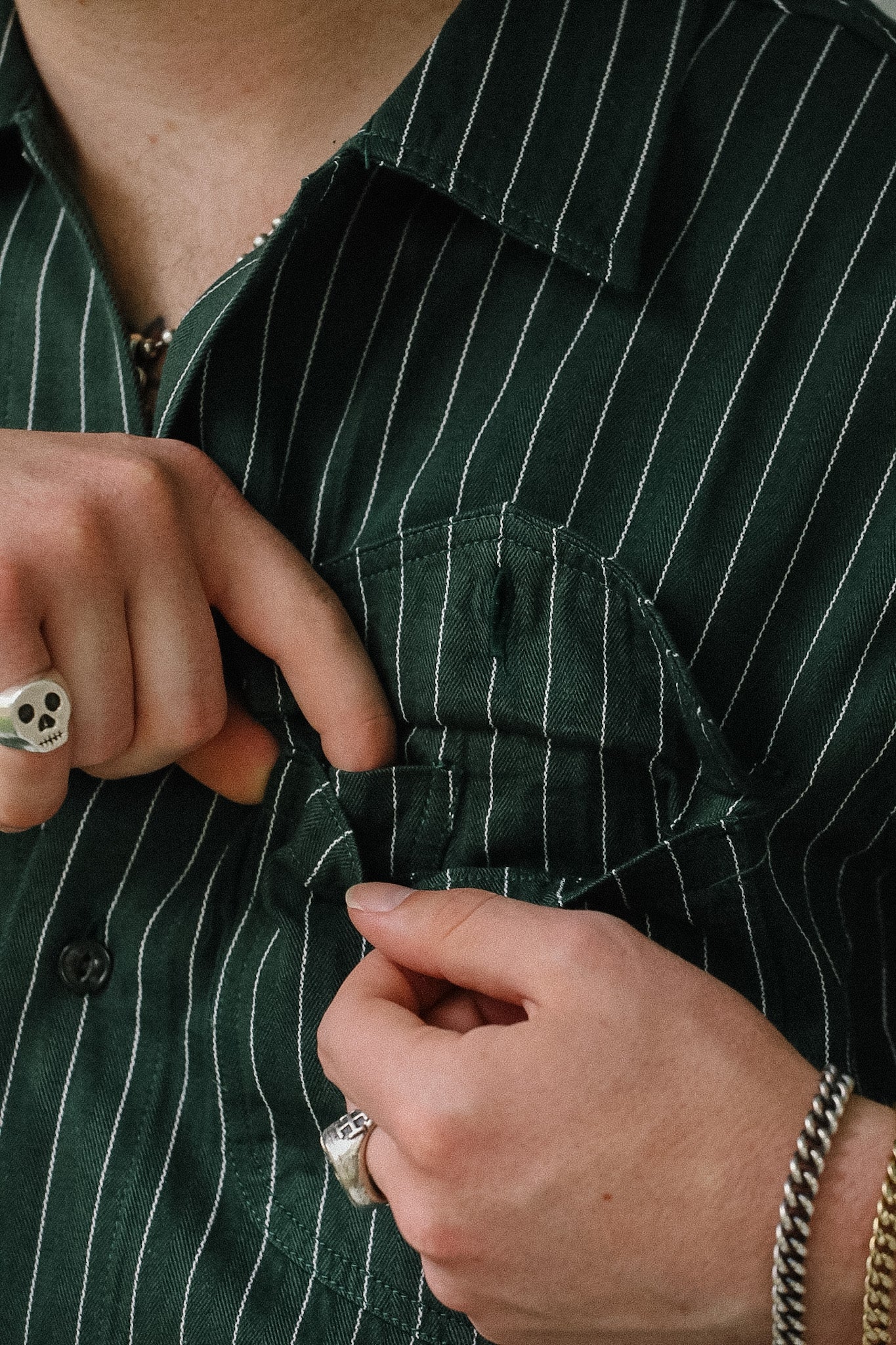 Person buttoning a green pinstripe shirt with close-up of hands and clothing details.