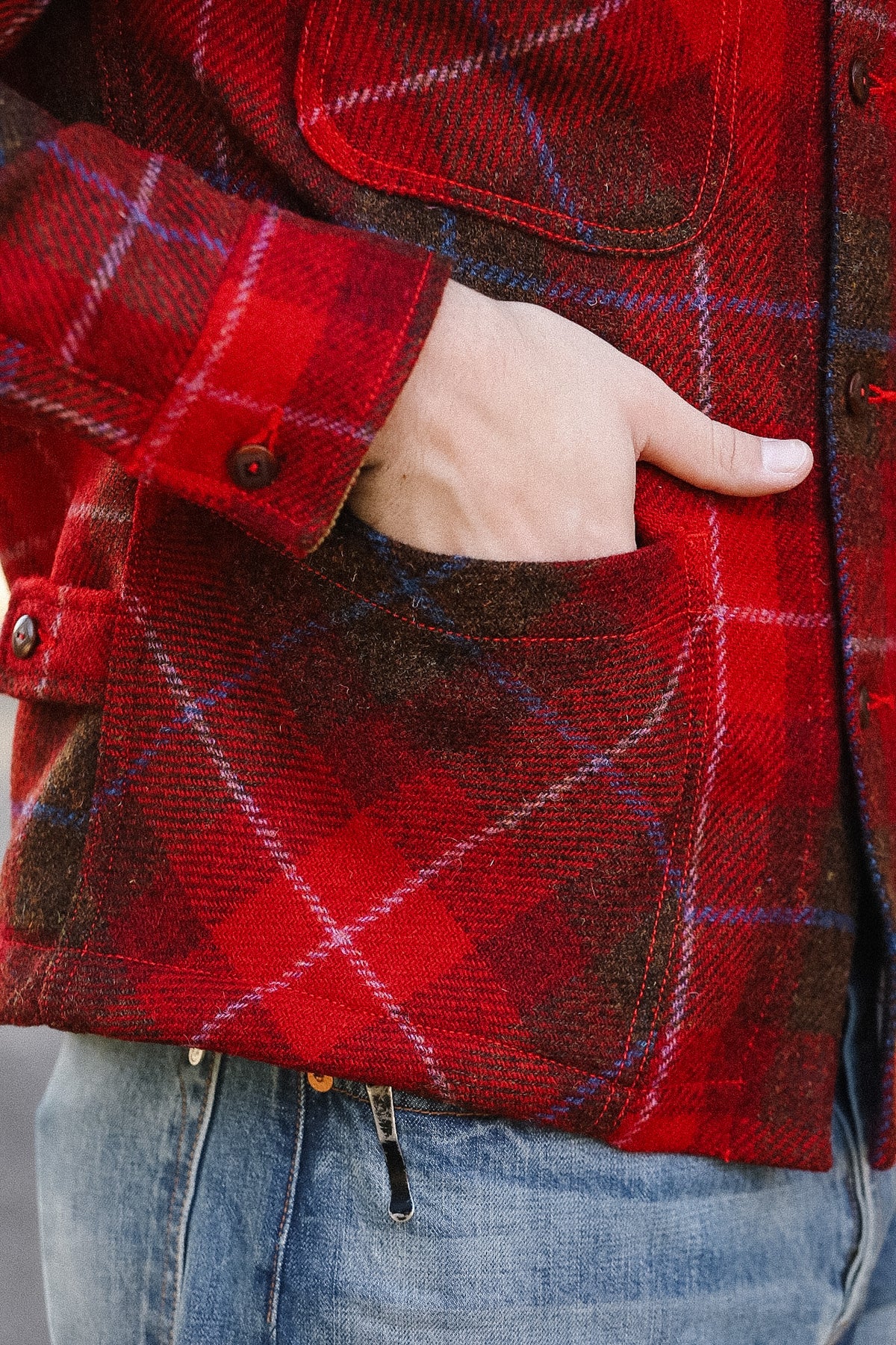 Red plaid jacket with a hand in the pocket, wearing blue jeans.