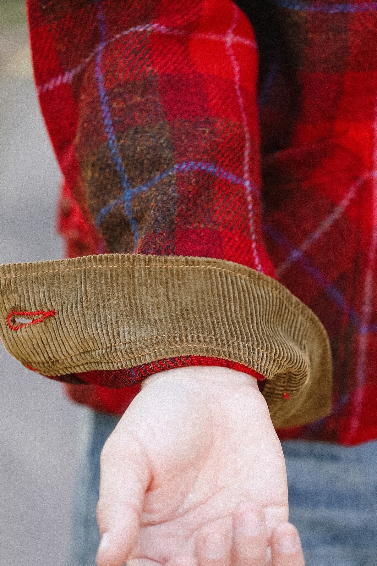 Close-up of a child's hand wearing brown corduroy shoes with a red plaid shirt.