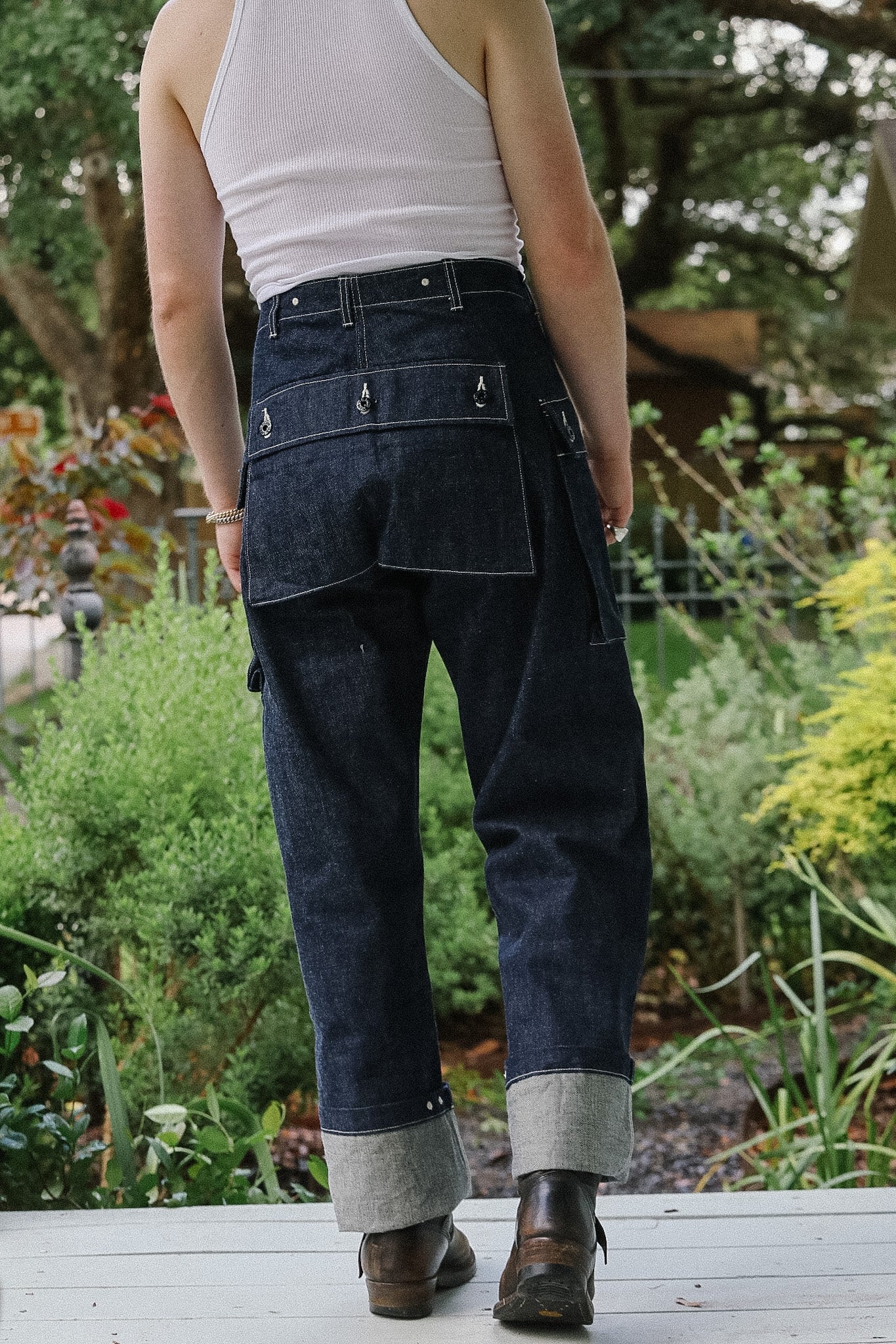 Person wearing dark blue jeans and a white tank top standing in a garden.