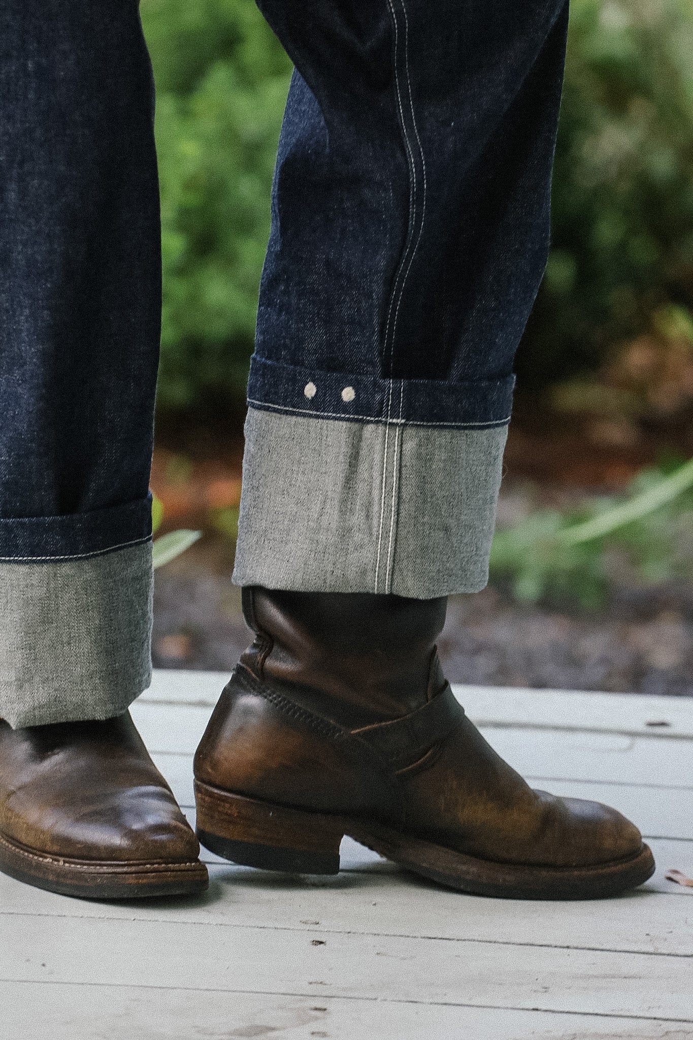 Brown leather boots worn with rolled-up jeans on a wooden floor.
