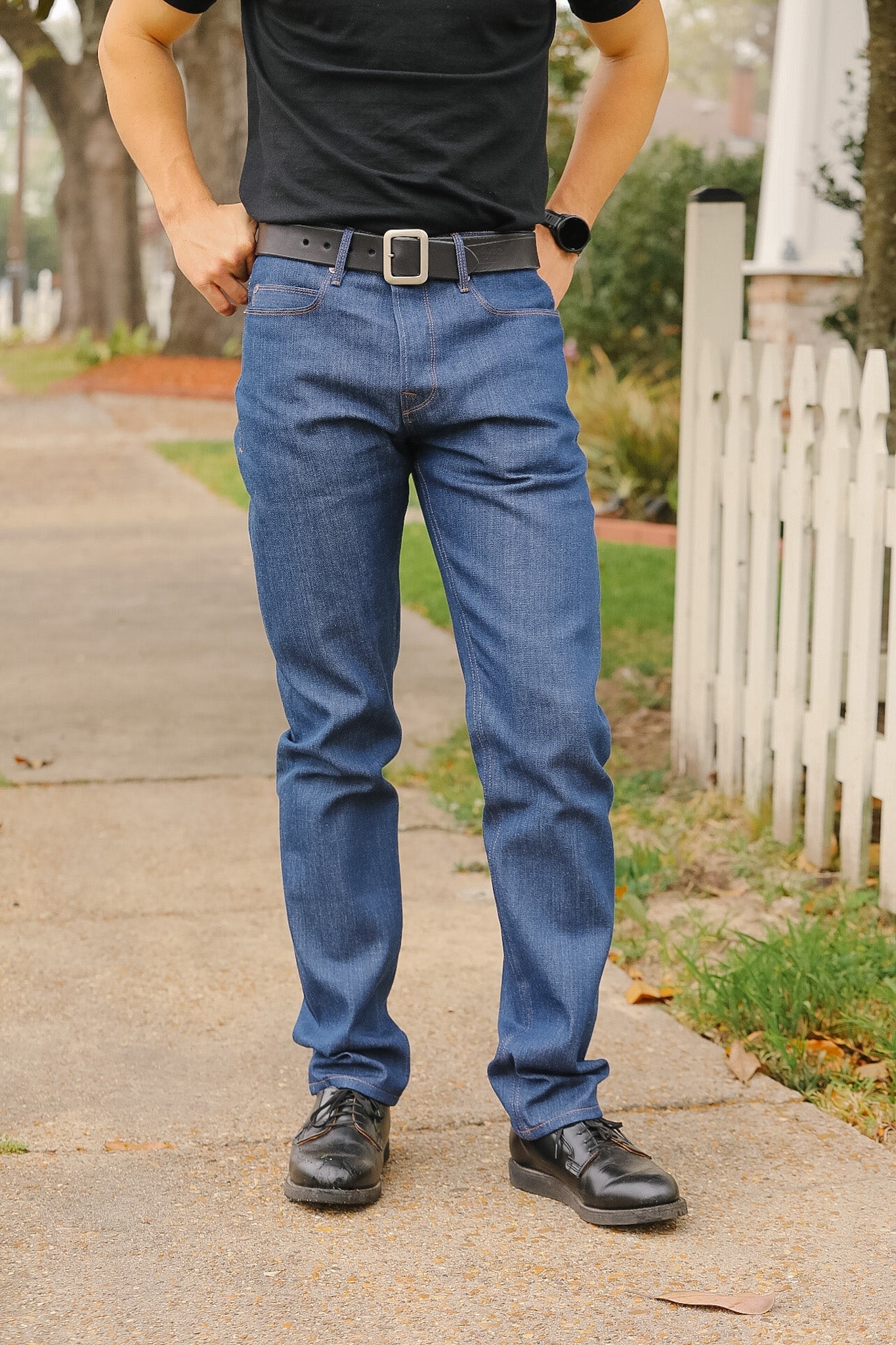 Person wearing blue jeans and black shoes on a sidewalk.