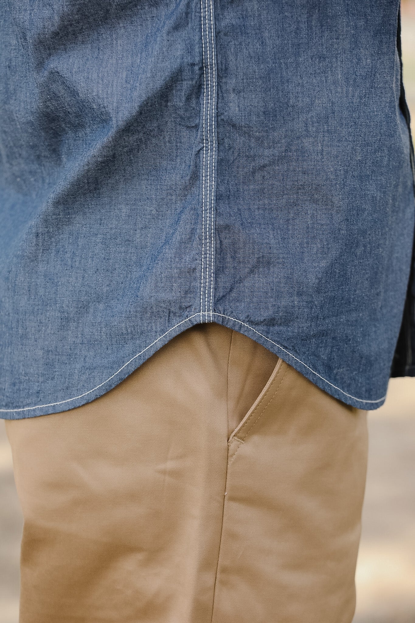 Close-up of a person wearing a blue denim shirt over a beige jacket.