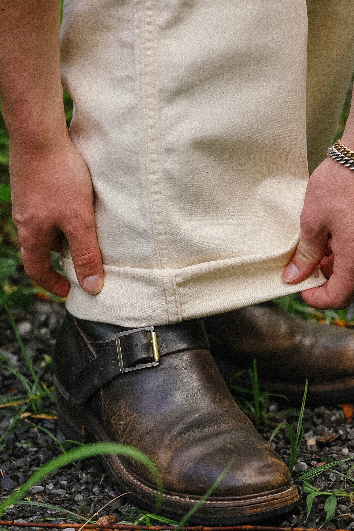 Person wearing a white apron over a beige shirt with a brown boot on a natural background