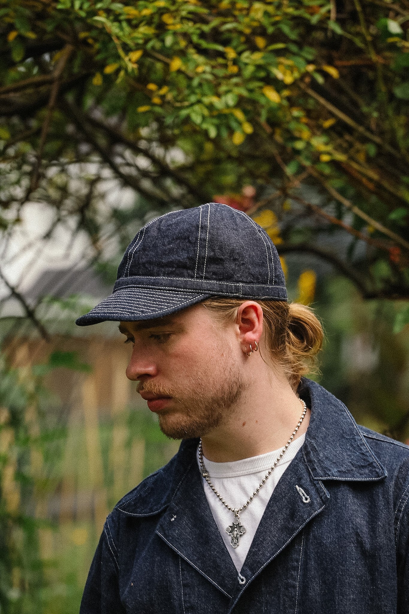 Man wearing a denim cap and coat outdoors with trees in the background