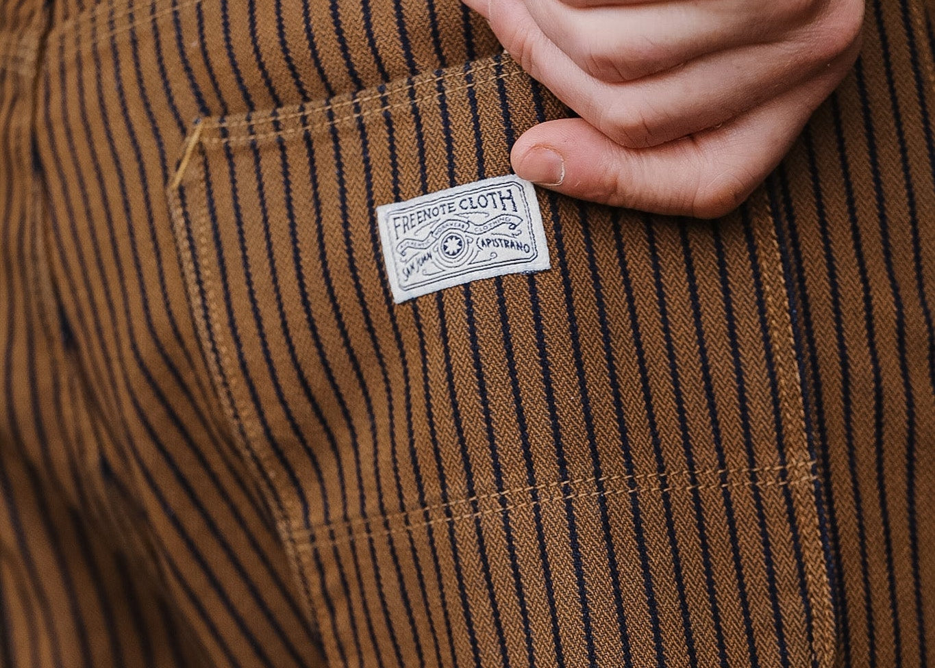 Close-up of brown striped pants with a brand label on the pocket.