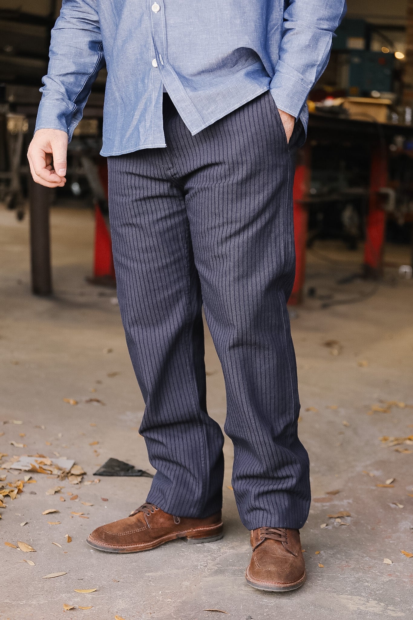 Person wearing a blue shirt and gray pinstripe pants standing in an outdoor setting.