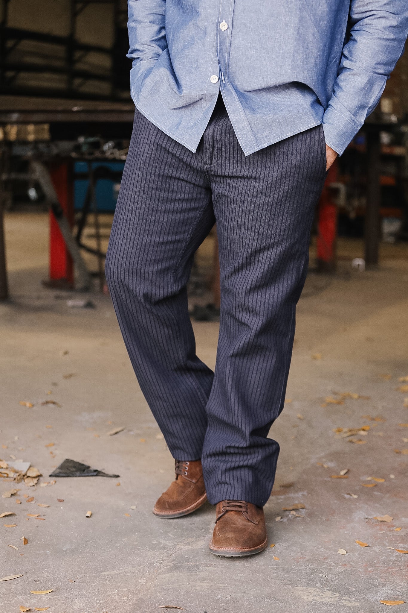 Person wearing a blue shirt and dark pinstripe pants standing on a concrete floor.