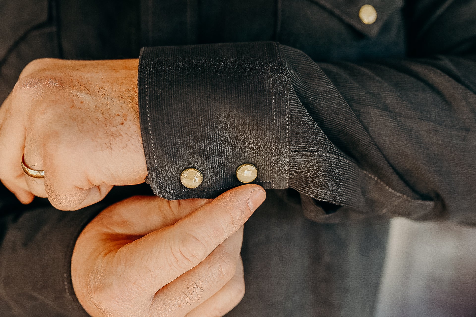 Close-up of a hand fastening metal snap buttons on a dark corduroy shirt cuff, rustic style