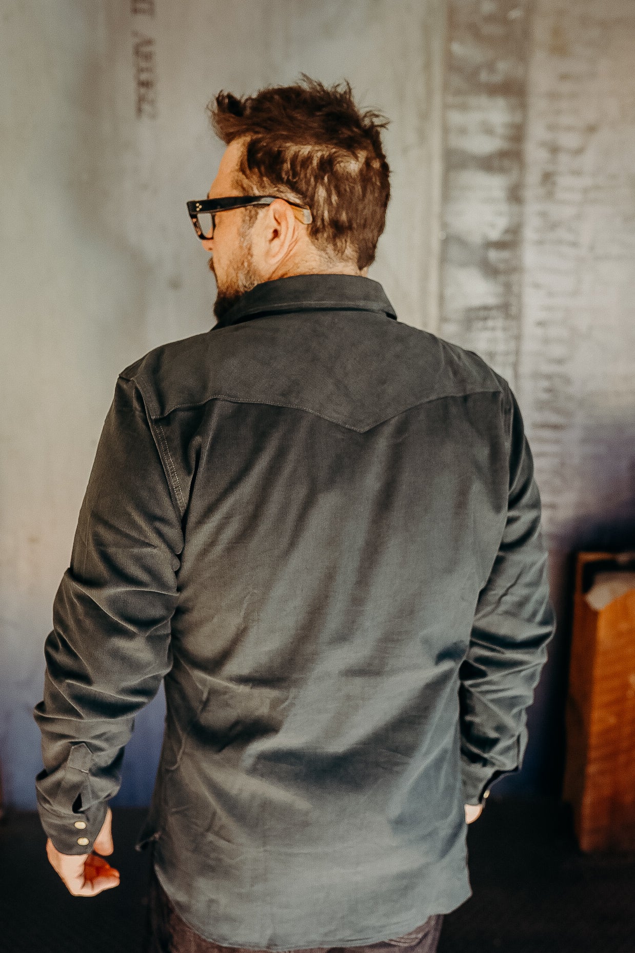 Man wearing black long-sleeve rugged work shirt in industrial setting, viewed from back