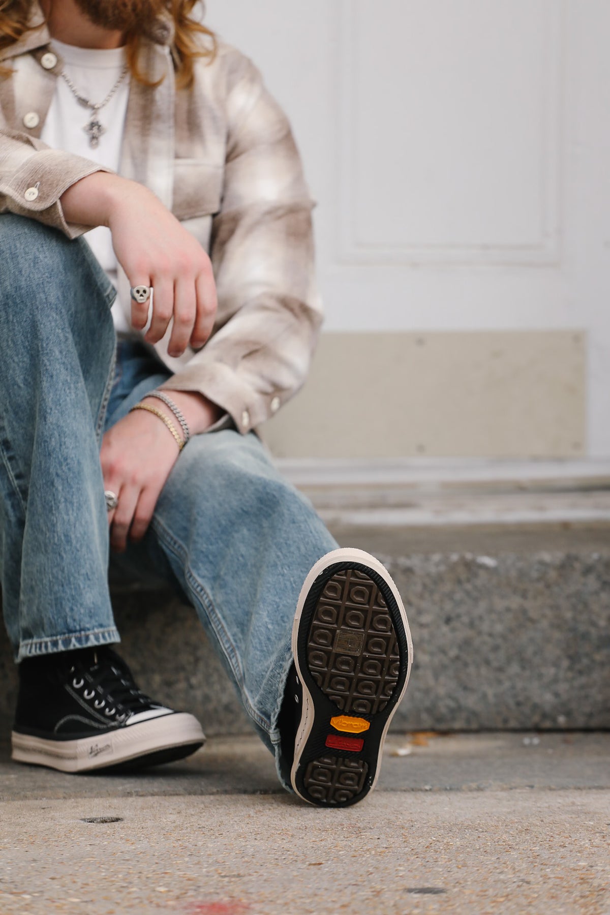 Person wearing black sneakers with a textured sole, sitting on a concrete surface.