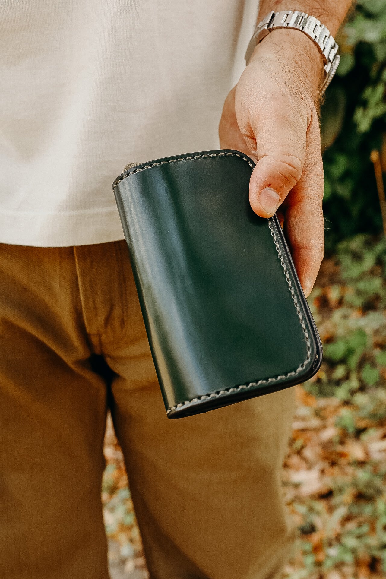 Man holding black leather wallet with hand-stitched edges outdoors near greenery