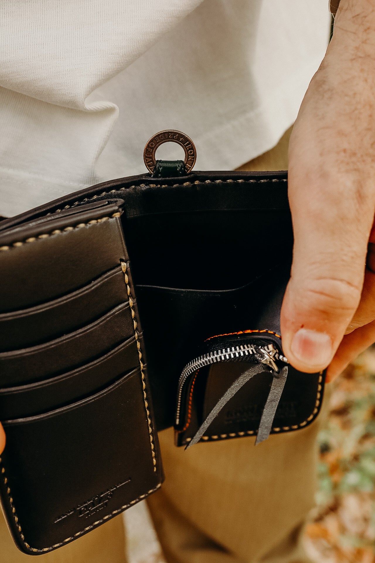Close-up of hands holding a black leather wallet with embossed logo and zipper coin pouch