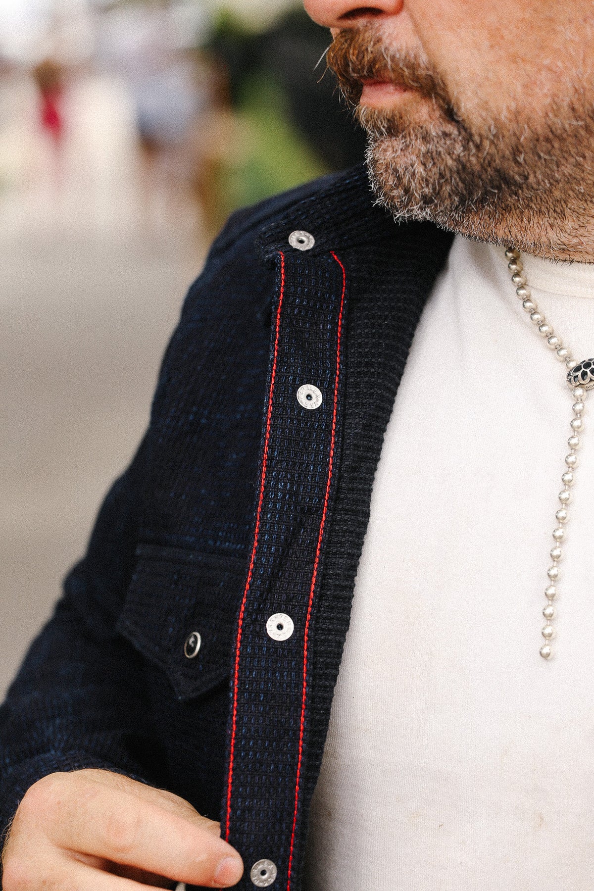 Close-up of a person wearing a dark jacket with red stitching and a white shirt.