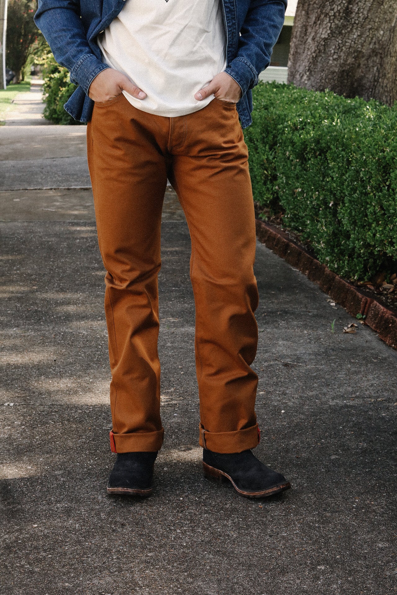 Person wearing brown work pants with black boots standing on a concrete sidewalk outdoors