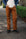Person wearing brown work pants with black boots standing on a concrete sidewalk outdoors