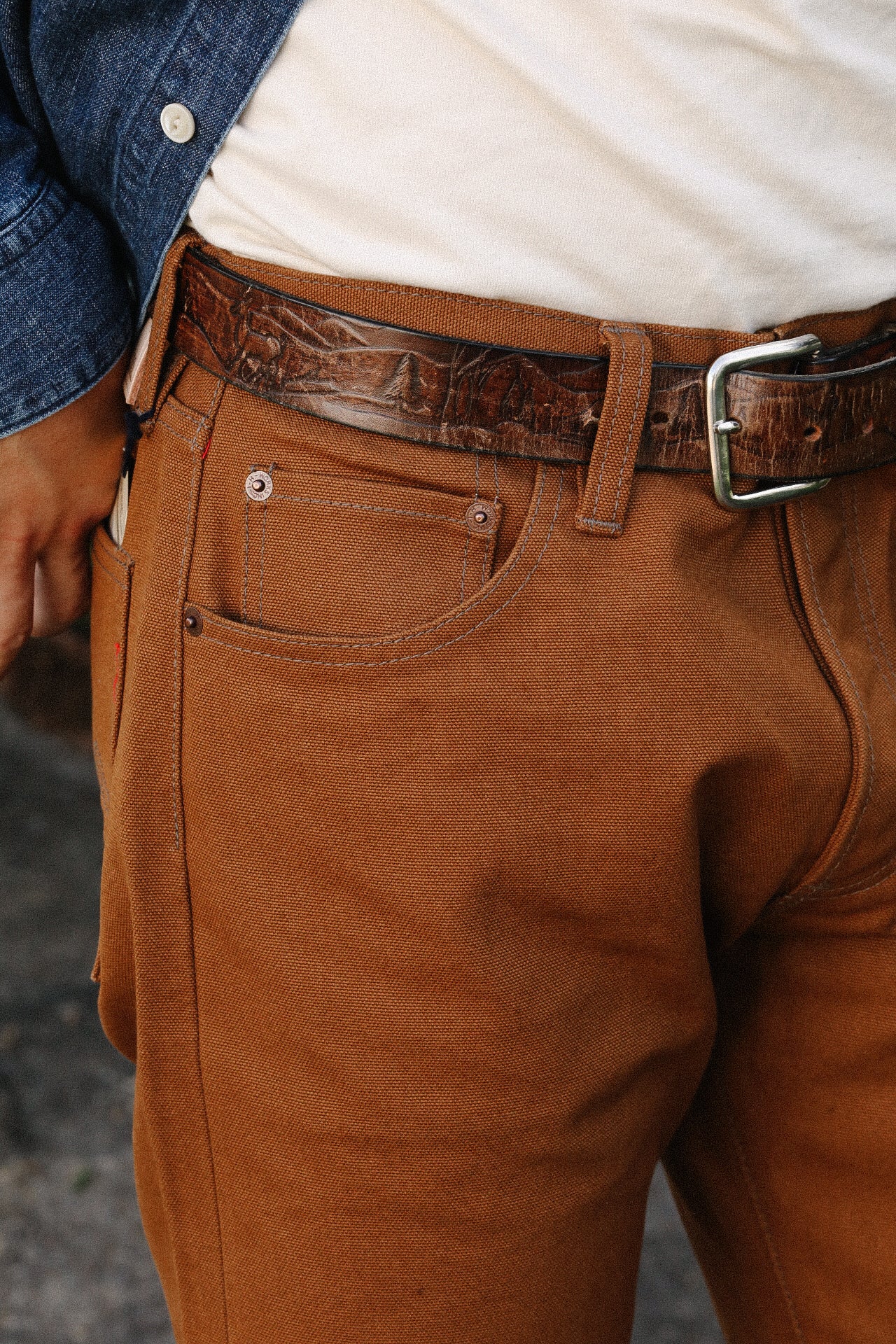 Close-up of rugged brown work pants with leather belt and denim jacket detail at Iron Shop Provisions