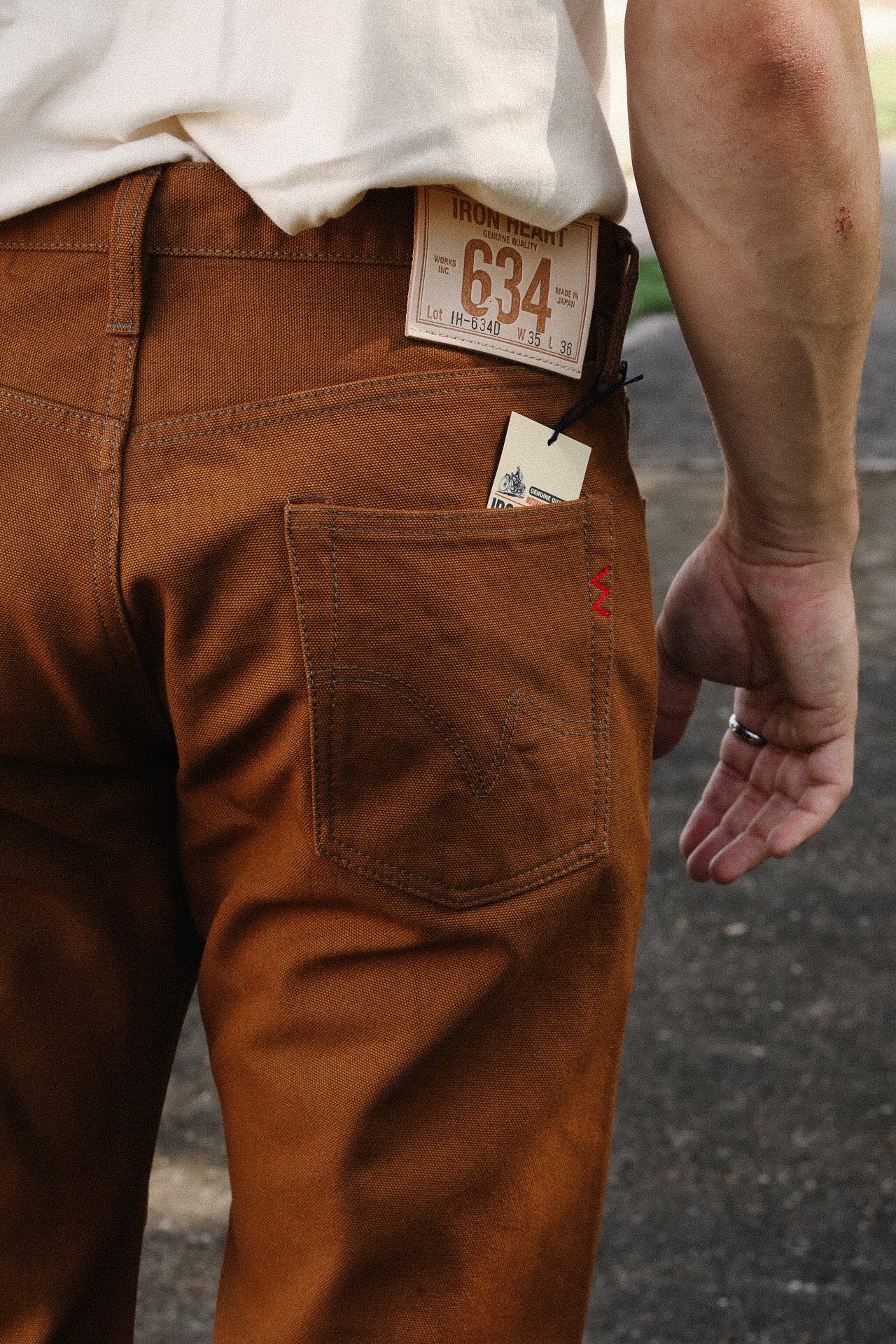 Close-up of brown Iron Heart 634 denim pants with leather label and back pocket detail, worn by a person outdoors