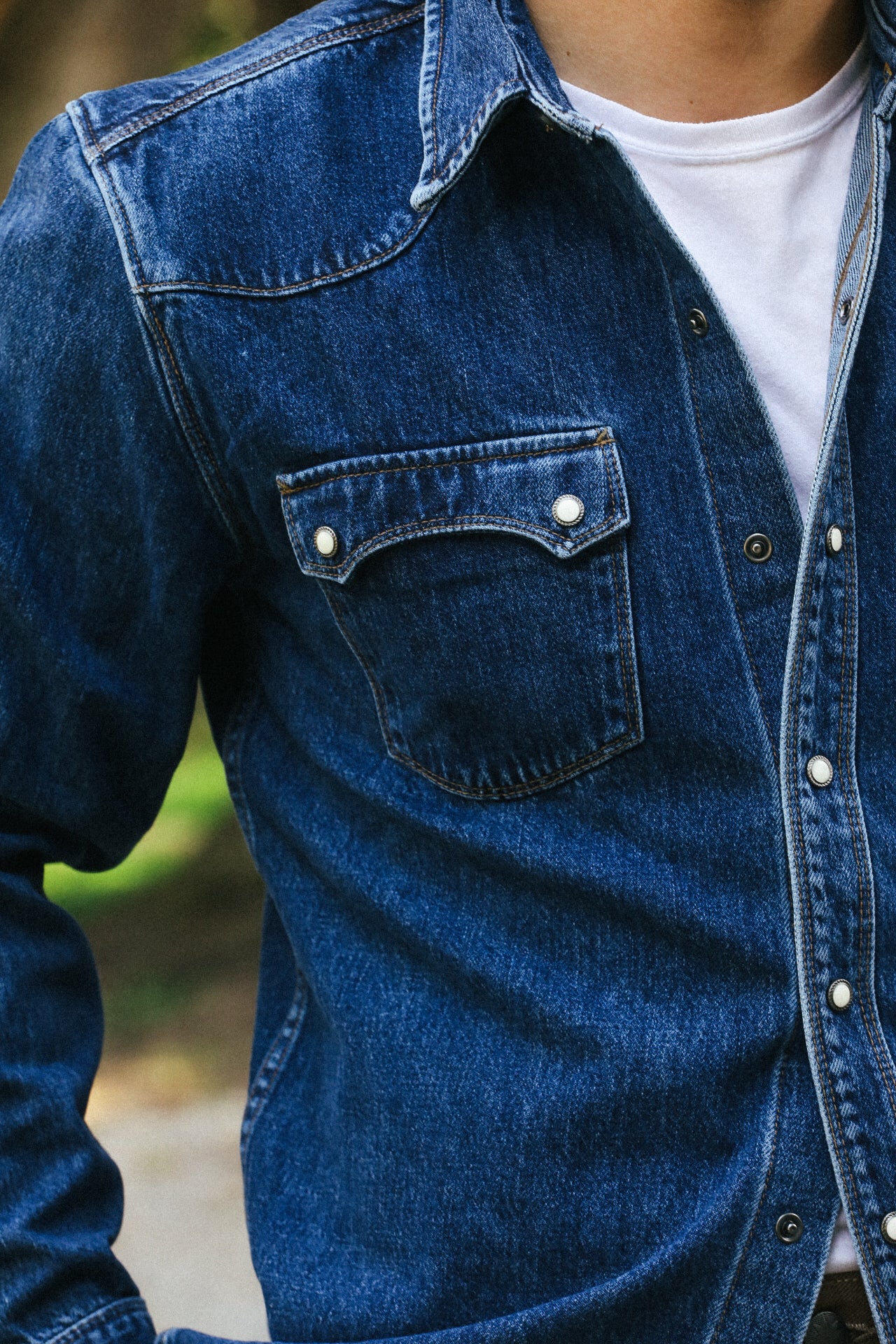 Close-up of man wearing dark blue denim jacket with white snap buttons over white t-shirt