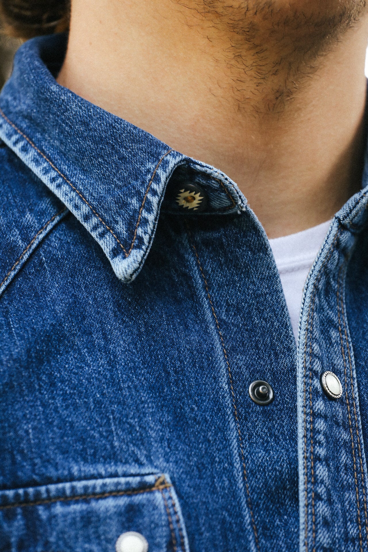Close-up of denim jacket collar with metal snap buttons and contrasting orange stitching over white shirt