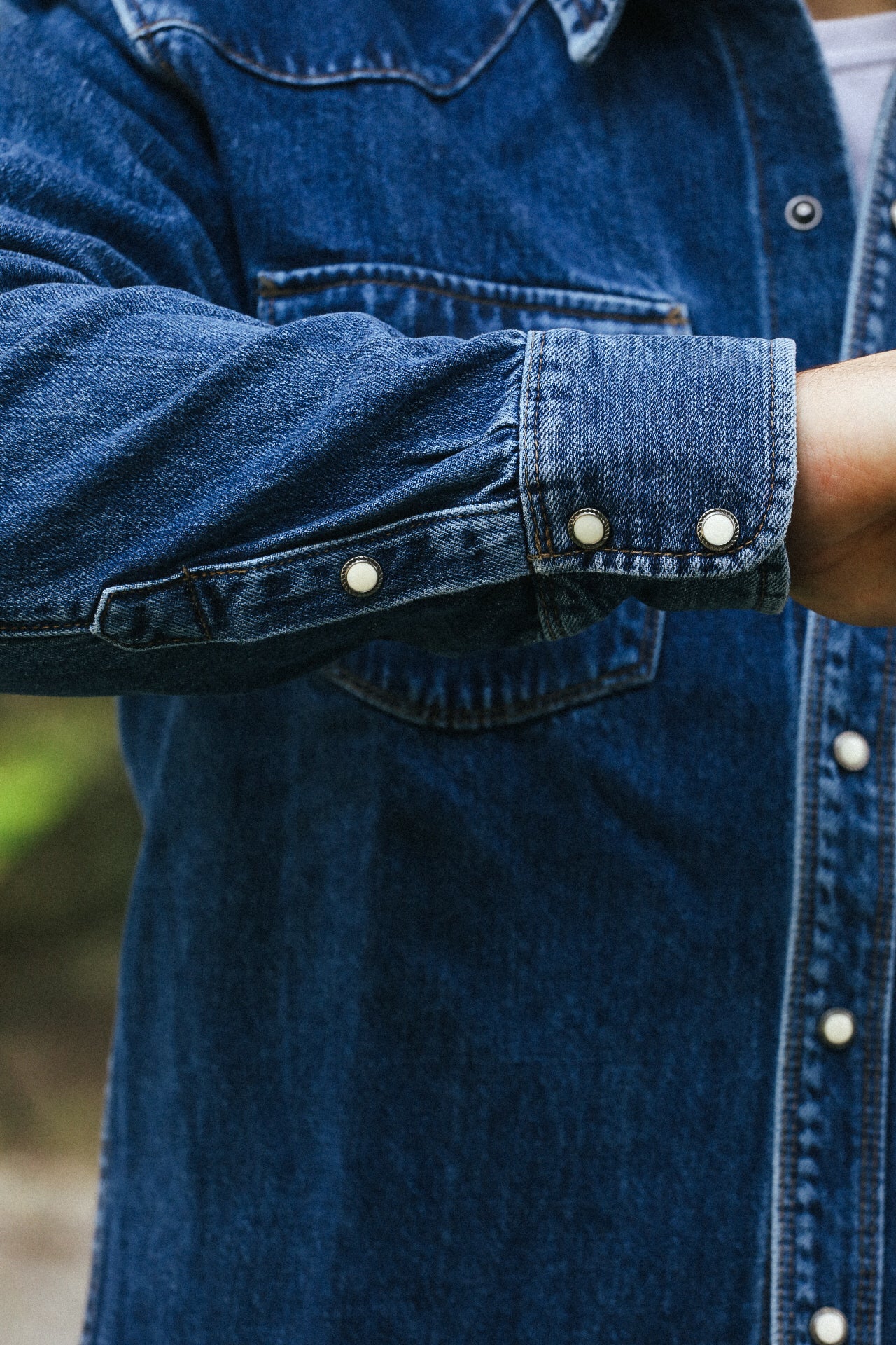 Close-up of denim shirt sleeve with metal snap buttons, showcasing rugged workwear style