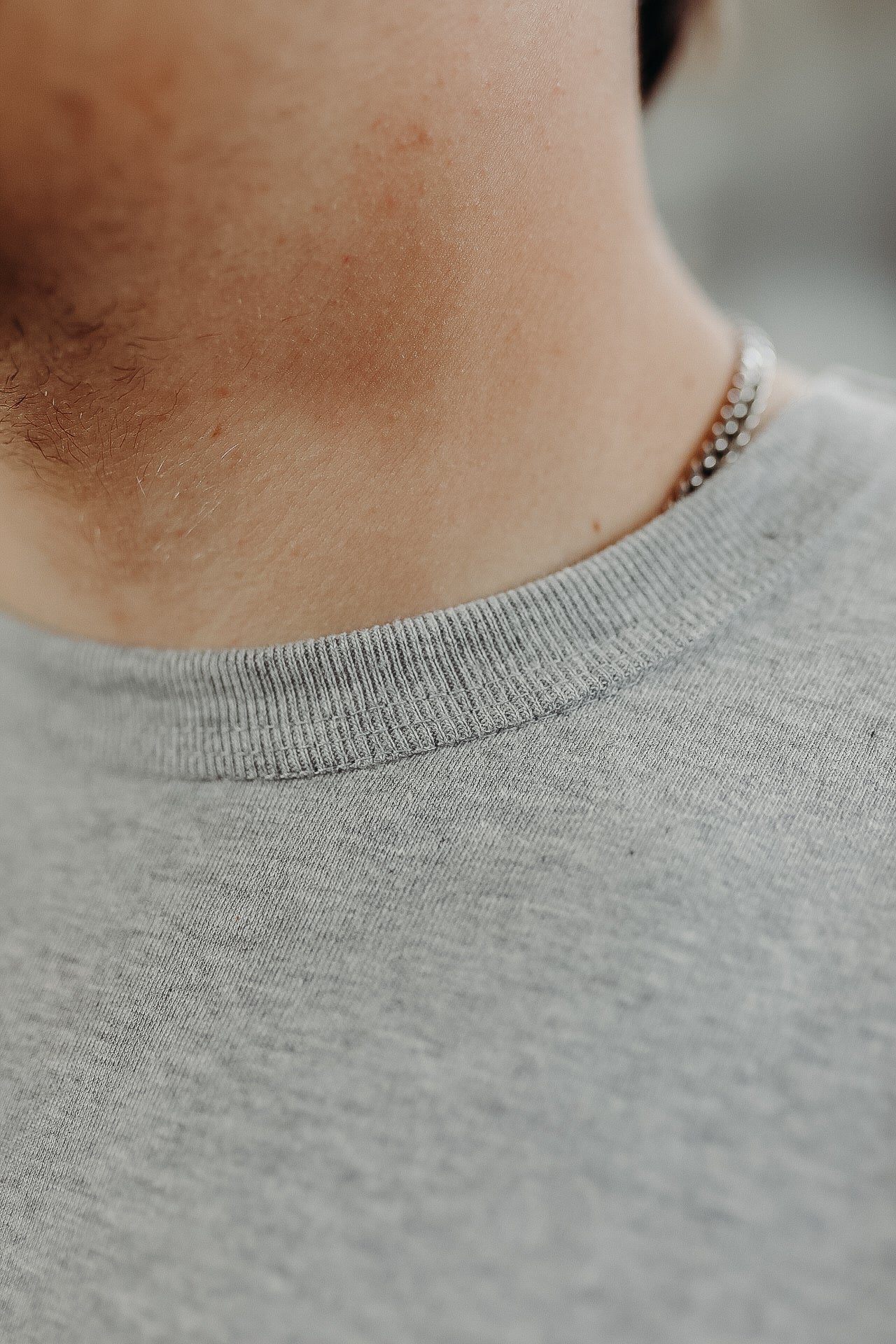 Close-up of a man's neck wearing a silver chain necklace and a grey crew neck t-shirt