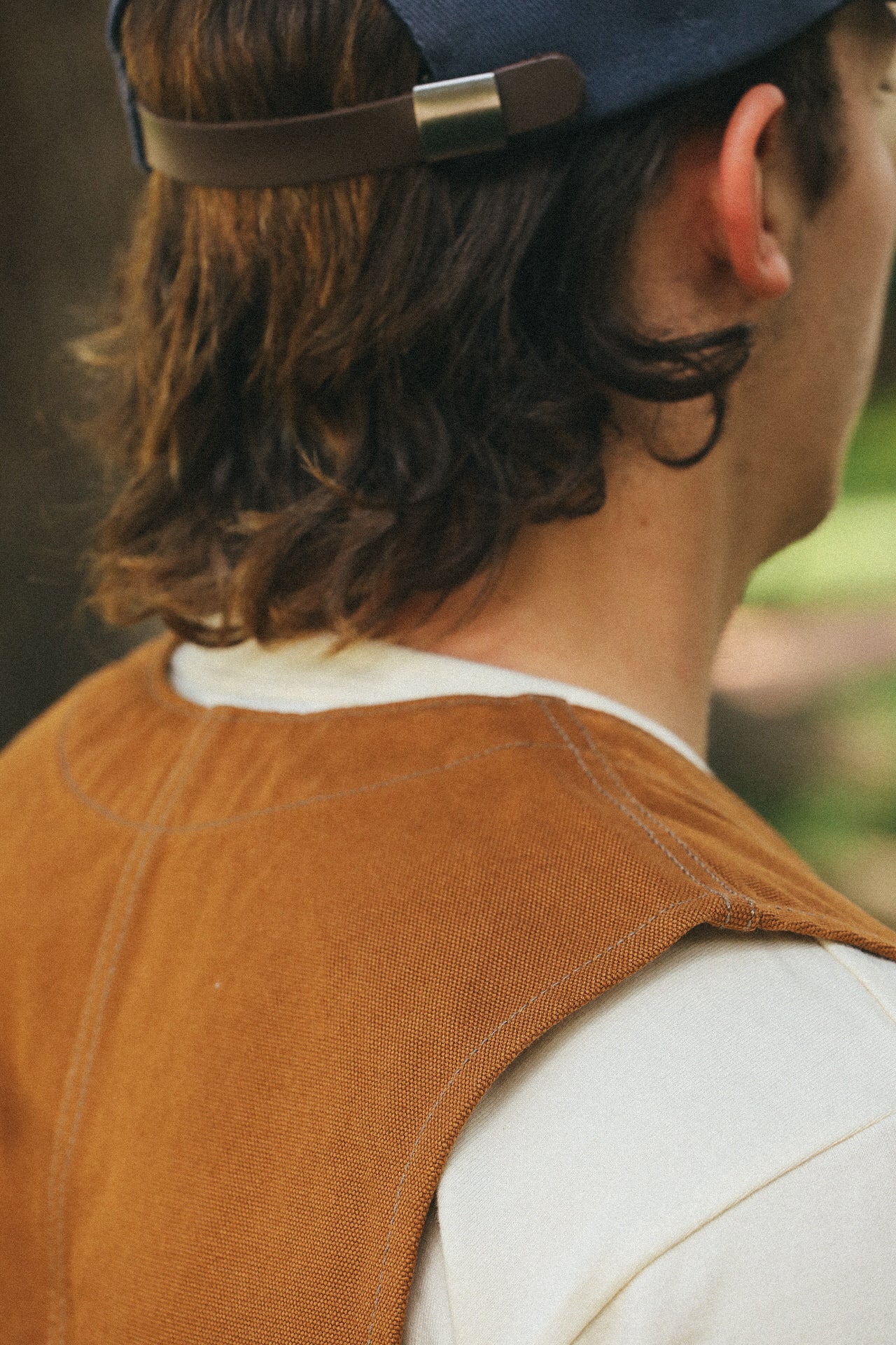 Close-up of a man wearing a brown work vest over a white shirt and a navy blue cap outdoors