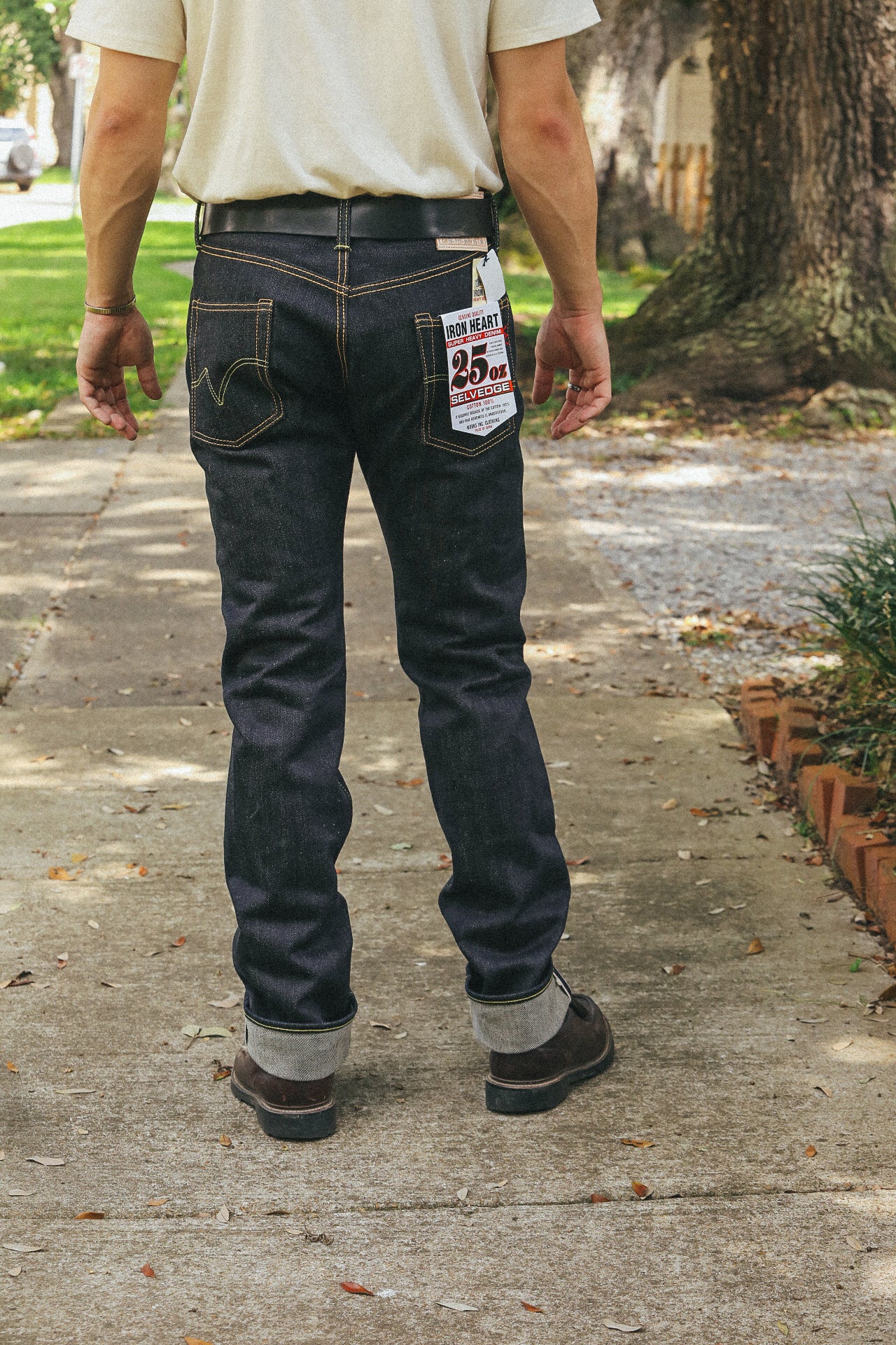Man wearing dark selvedge denim jeans with 25oz Iron Heart label walking on sidewalk outdoors