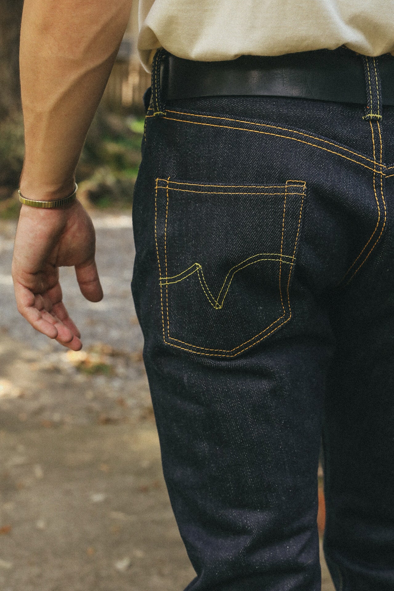 Close-up of a person wearing dark denim jeans with yellow stitching and a black leather belt