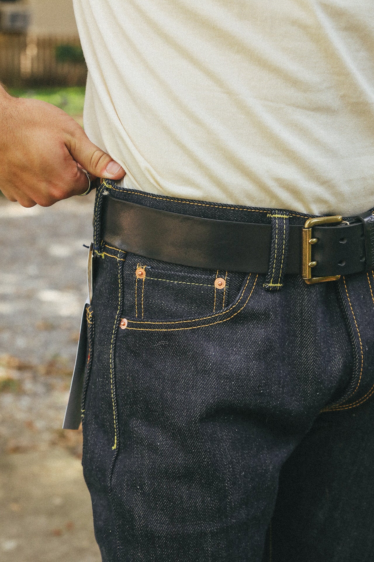 Close-up of person wearing dark denim jeans with yellow stitching and a black leather belt with brass buckle