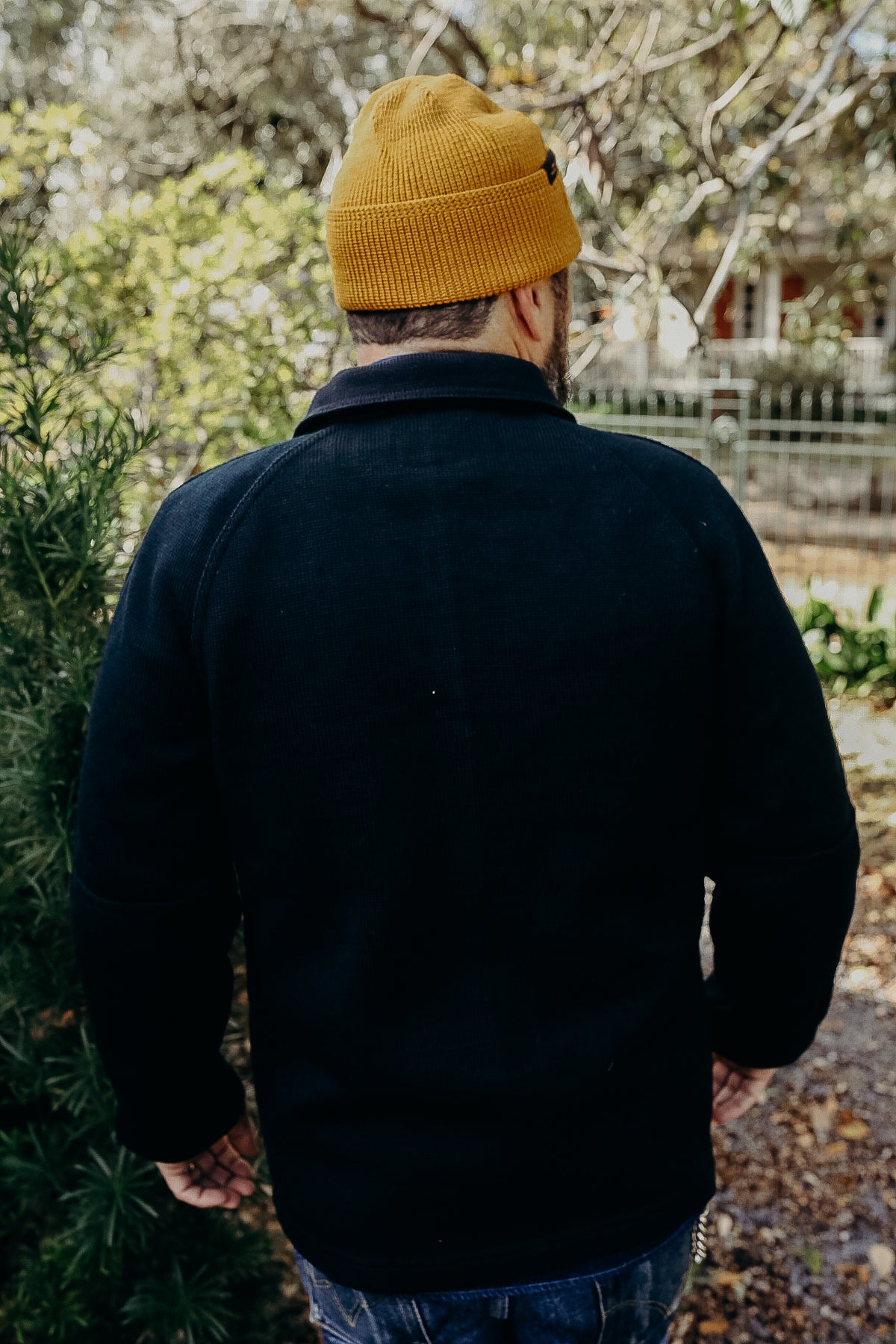 Man wearing mustard beanie and black jacket in outdoor garden setting