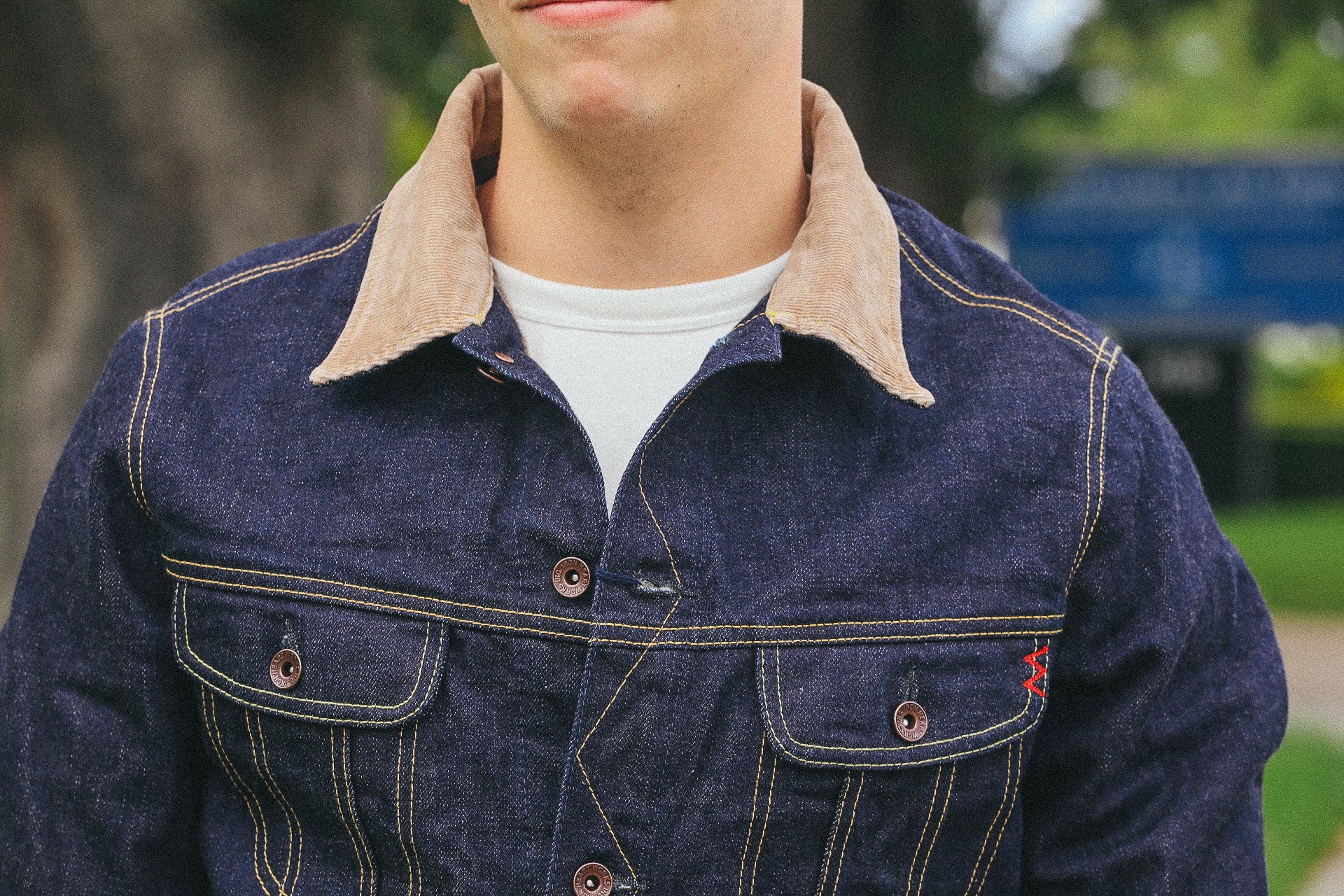 Man wearing a dark denim jacket with a tan corduroy collar and yellow stitching outdoors