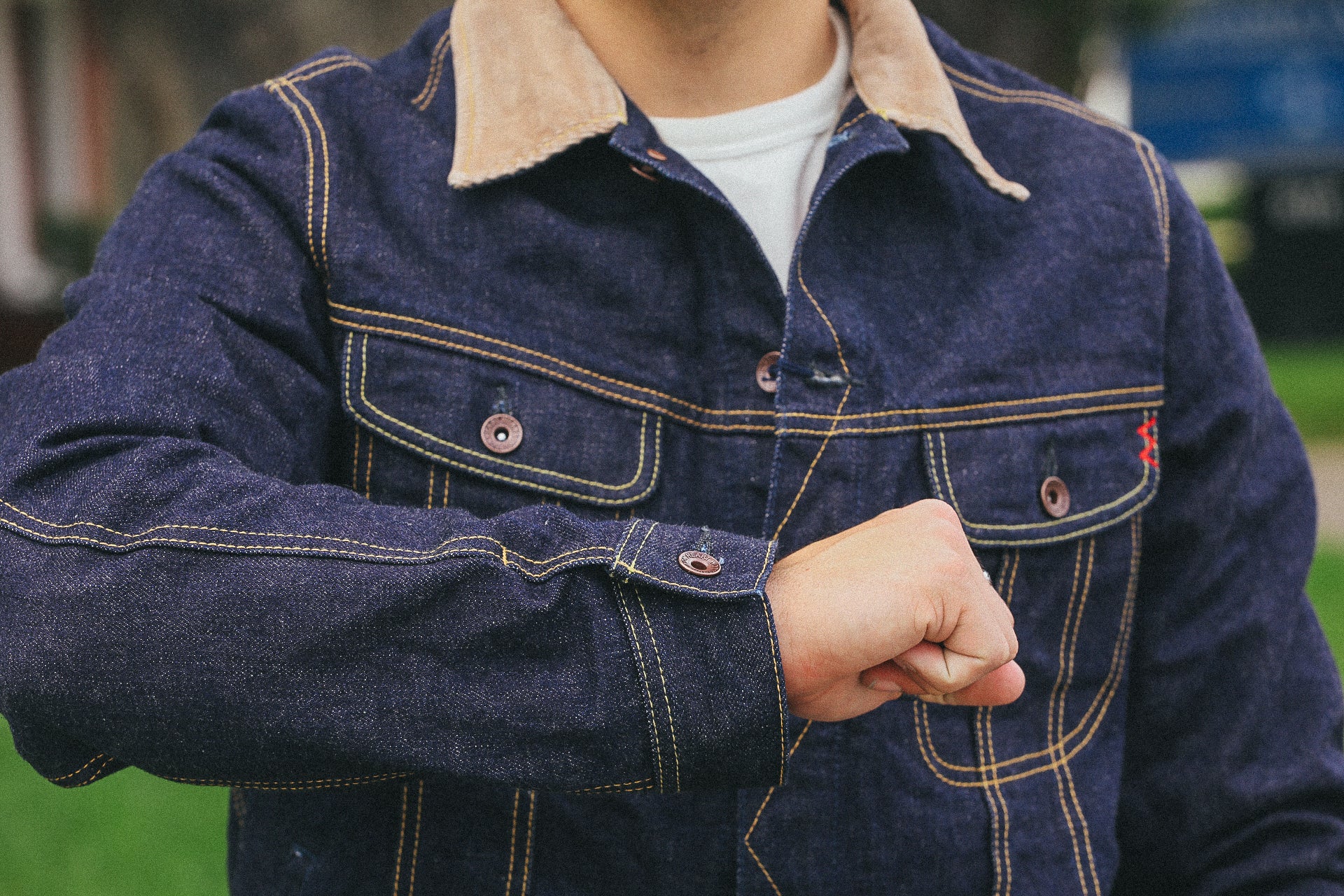 Person wearing dark denim jacket with contrast stitching and light collar outdoors