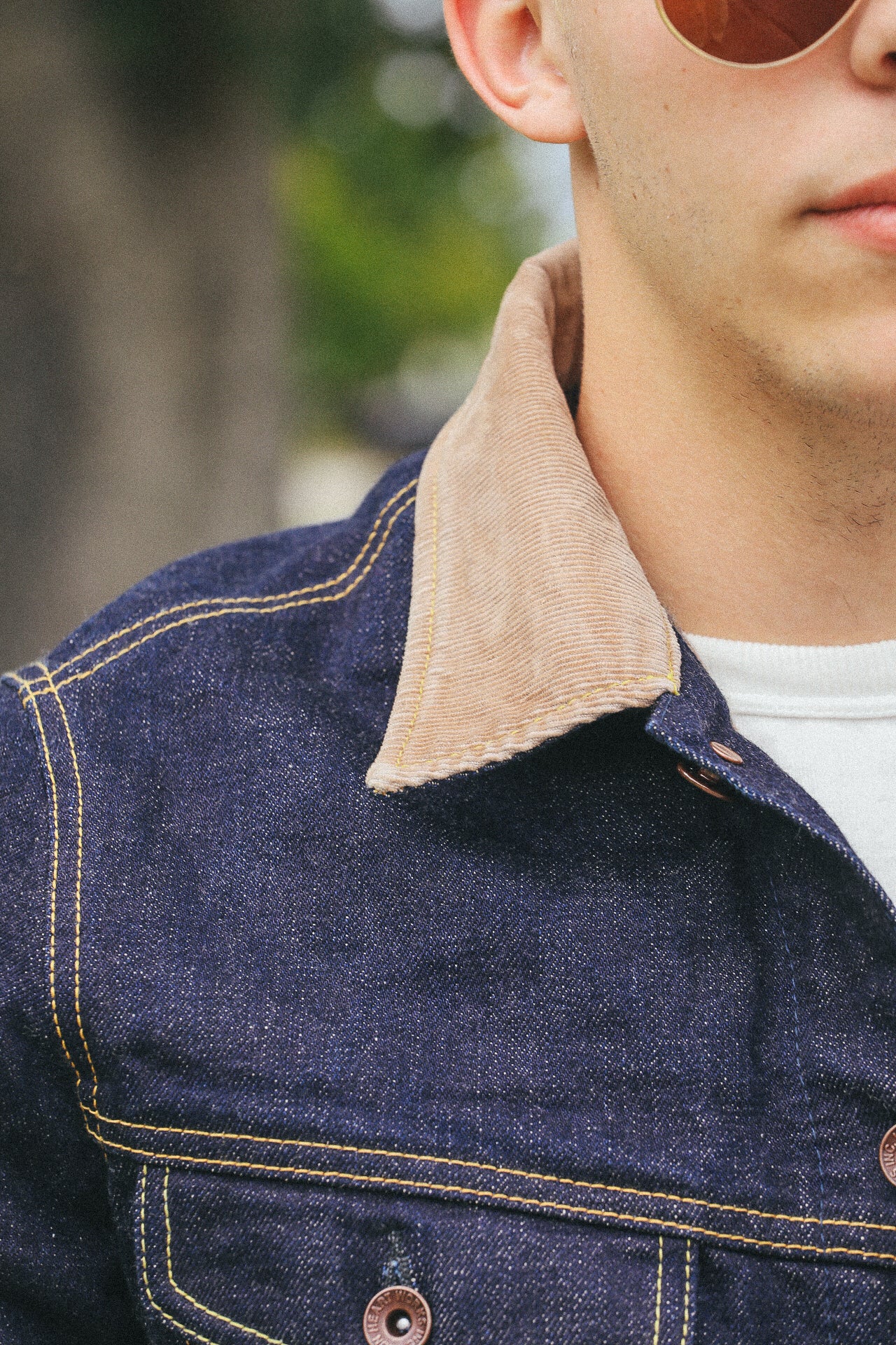 Close-up of a man wearing a dark denim jacket with beige corduroy collar and sunglasses