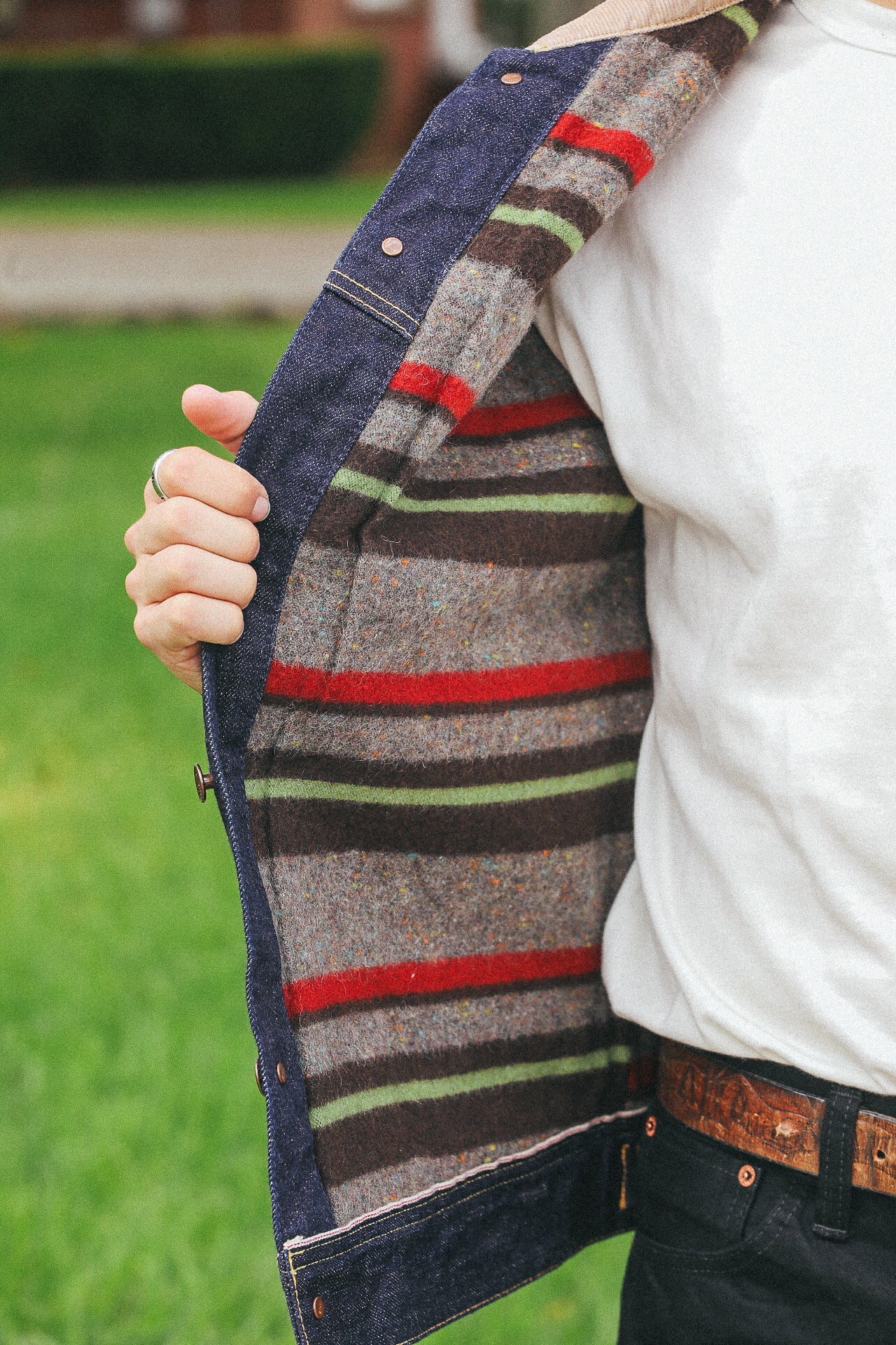 Close-up of person wearing denim jacket with striped wool lining, white shirt, and leather belt outdoors
