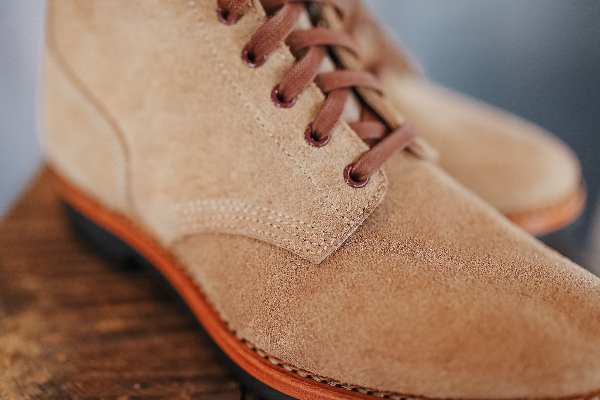 Close-up of a tan suede shoe with brown laces on a wooden surface.