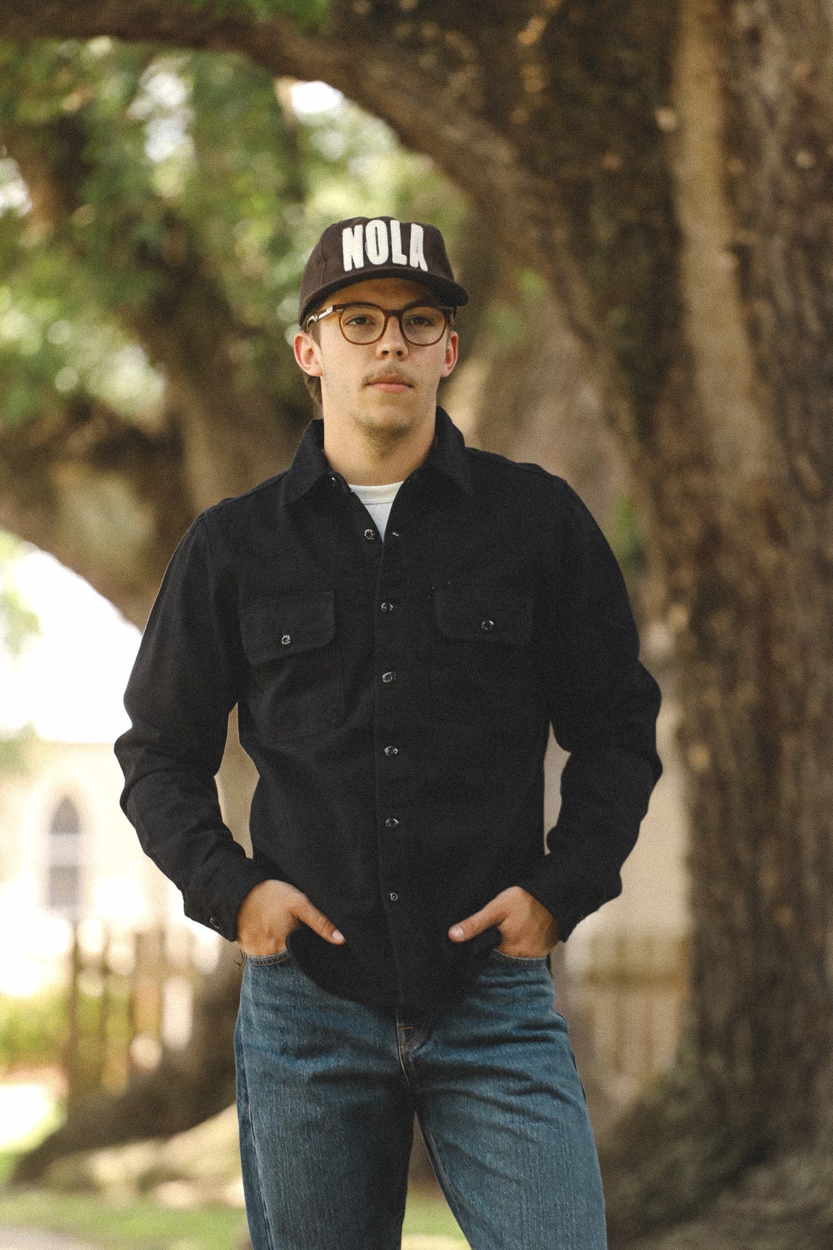 Person wearing a black jacket and cap with 'NOLA' text, standing outdoors.