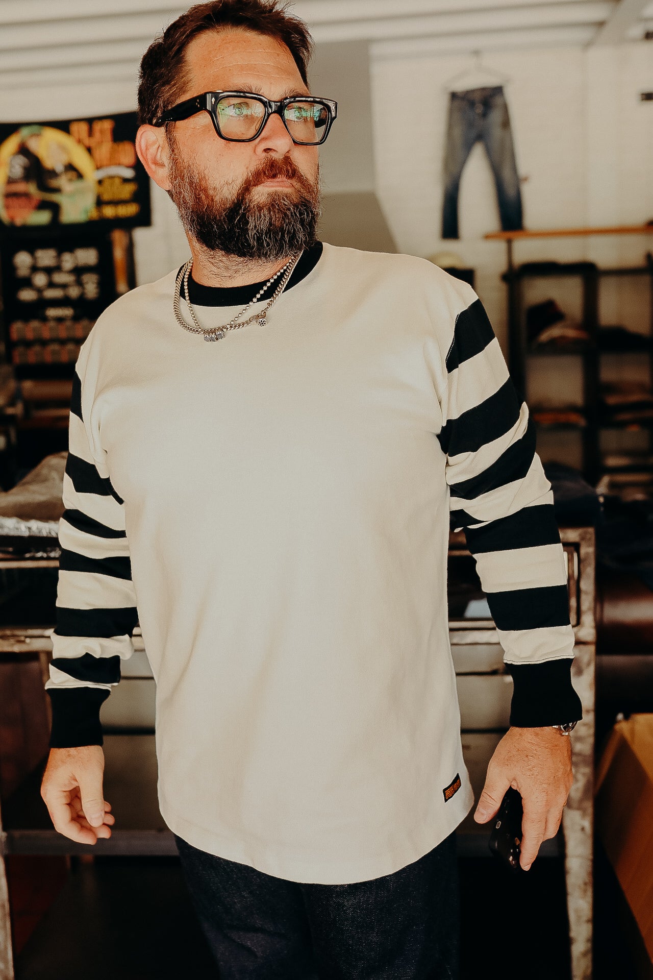 Bearded man wearing black and white striped long sleeve shirt and glasses in vintage-style clothing store