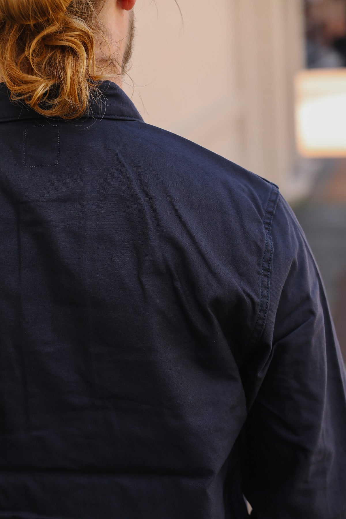 Close-up back view of a person wearing a dark navy blue work shirt or overshirt, with the fabric texture and shoulder seam visible.