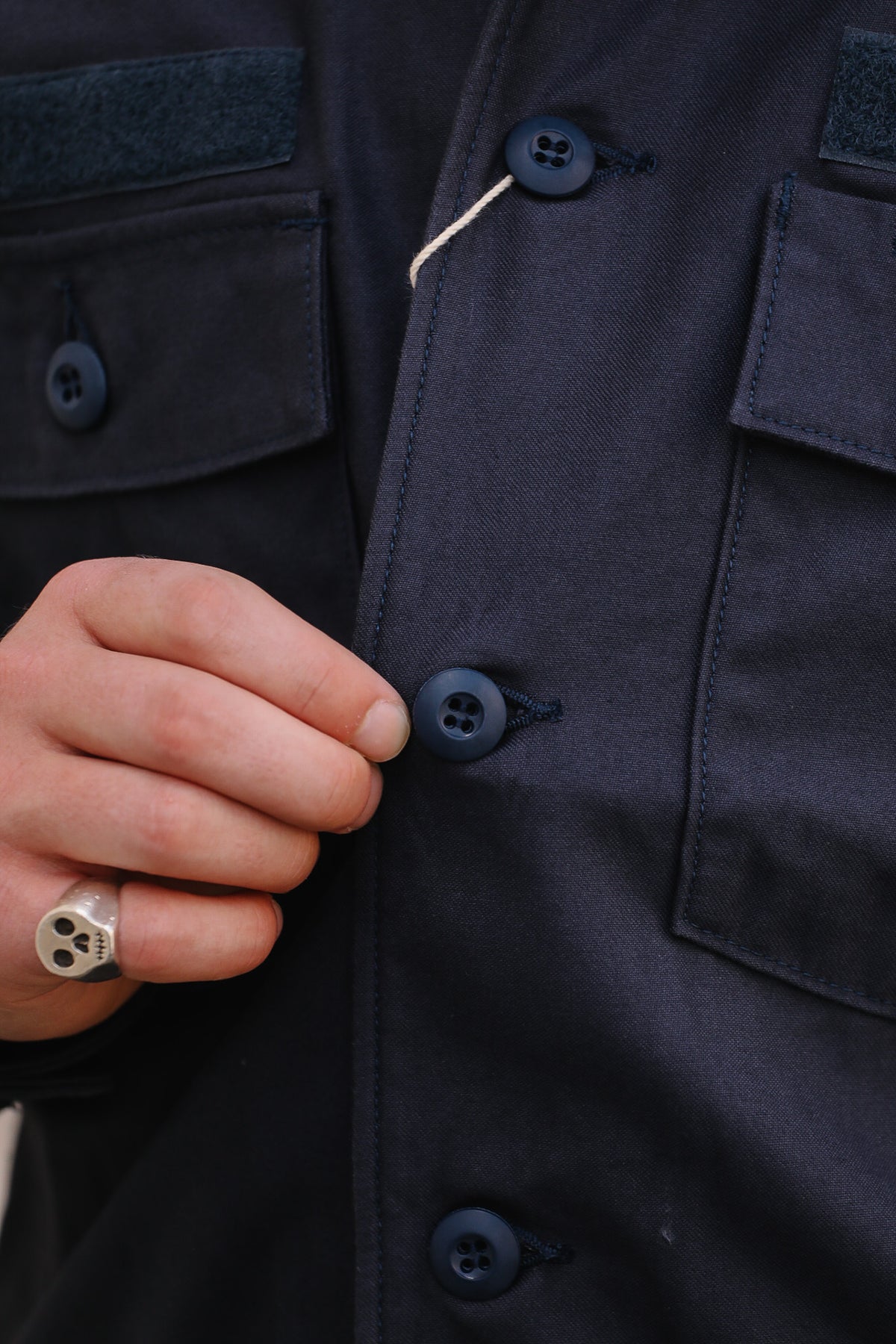 Close-up of a person's hand fastening a dark navy button on a matching navy utility jacket or overshirt.