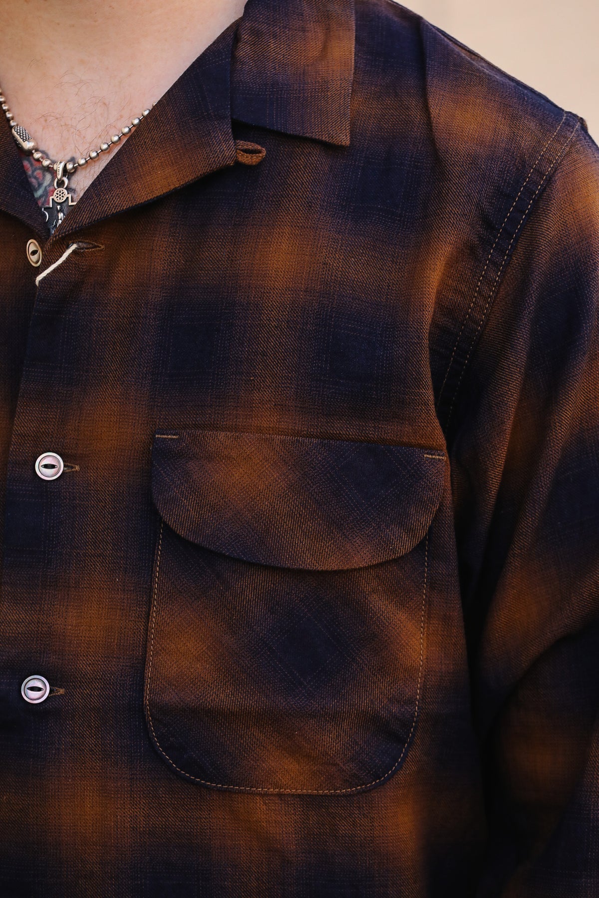 Close-up of a dark brown and black plaid button-up shirt with a chest pocket, worn by a model.