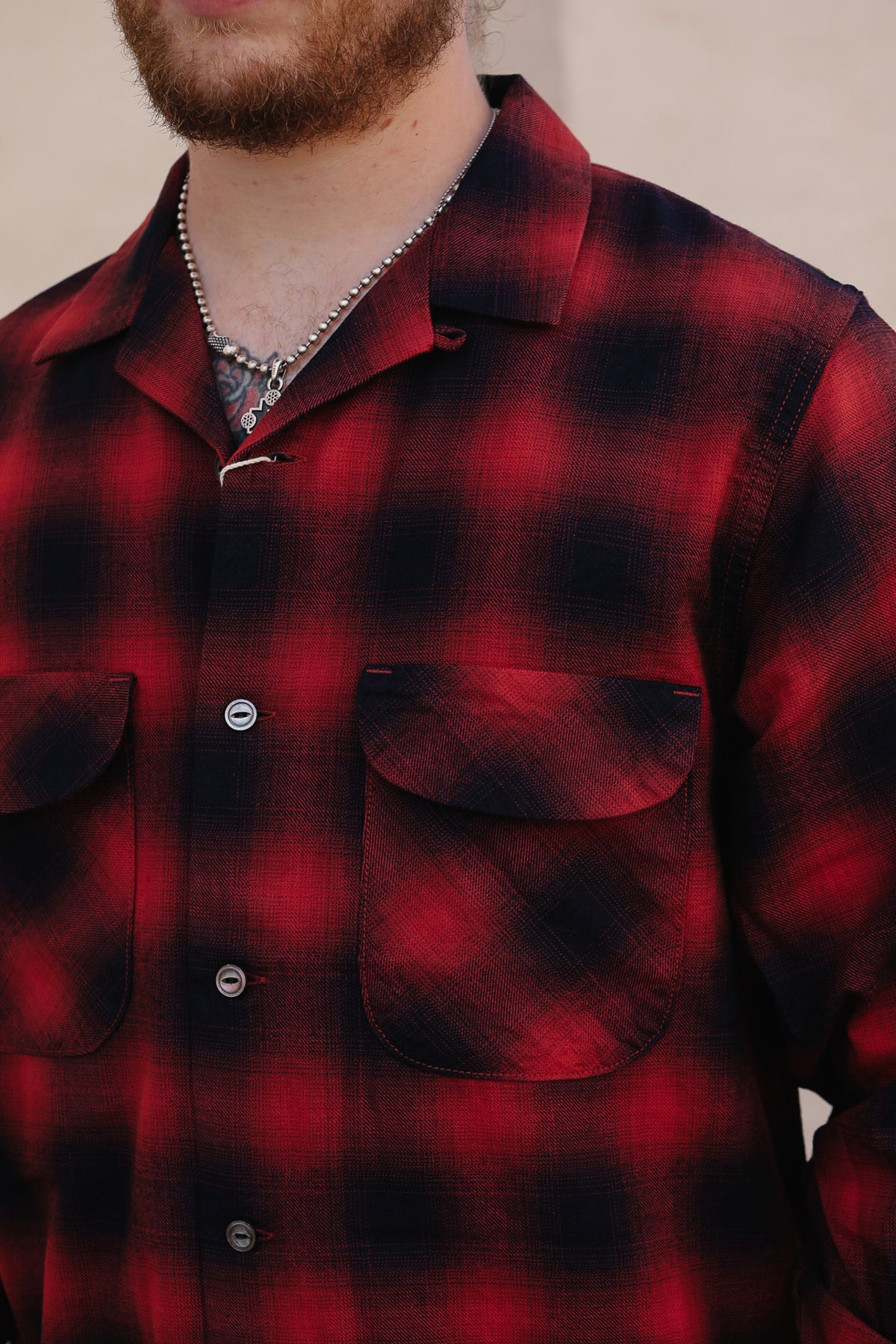A close-up of a man wearing a red and black plaid flannel button-up shirt with two chest pockets and silver buttons.