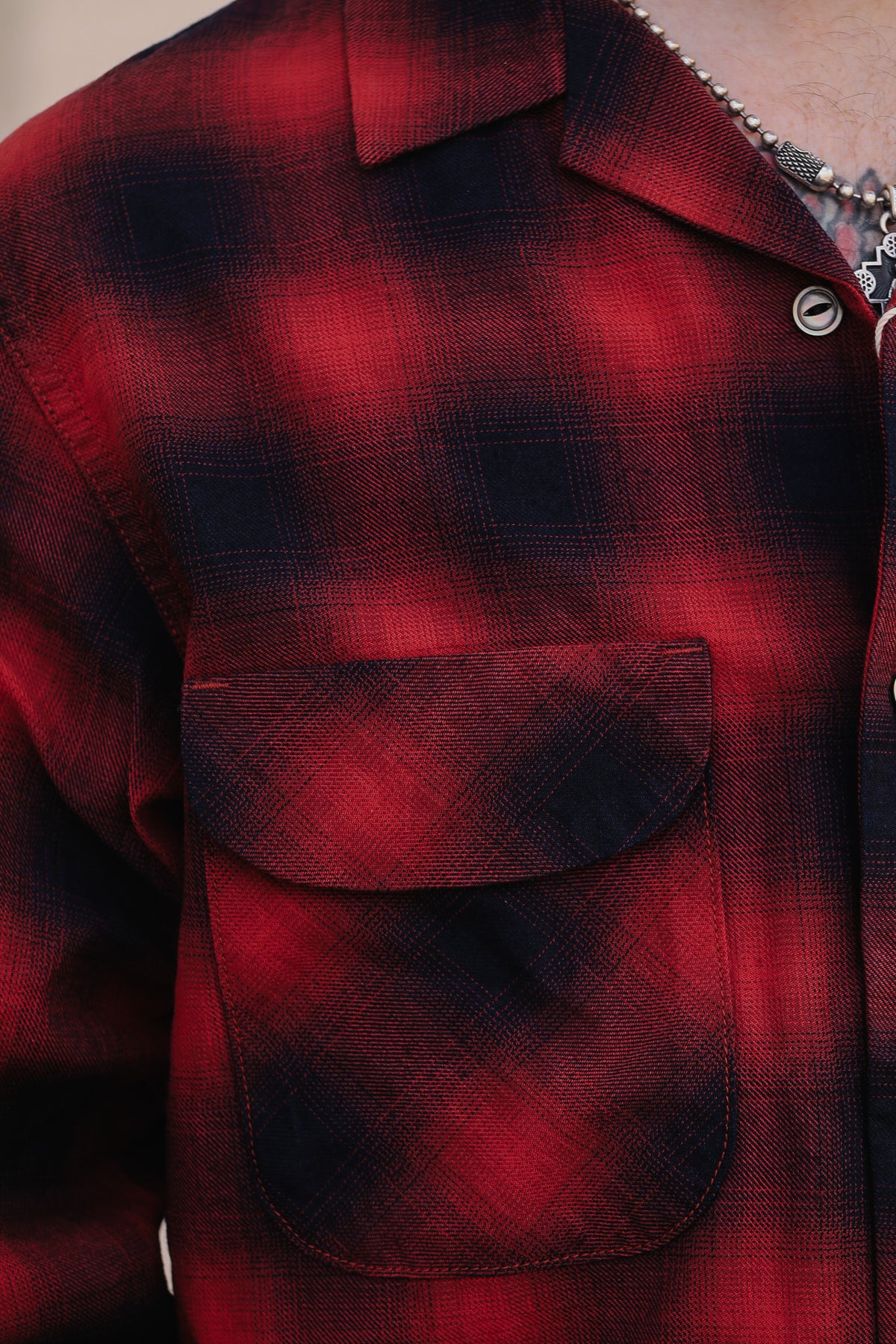 Close-up of a red and black plaid flannel shirt with a chest pocket, worn by a model.