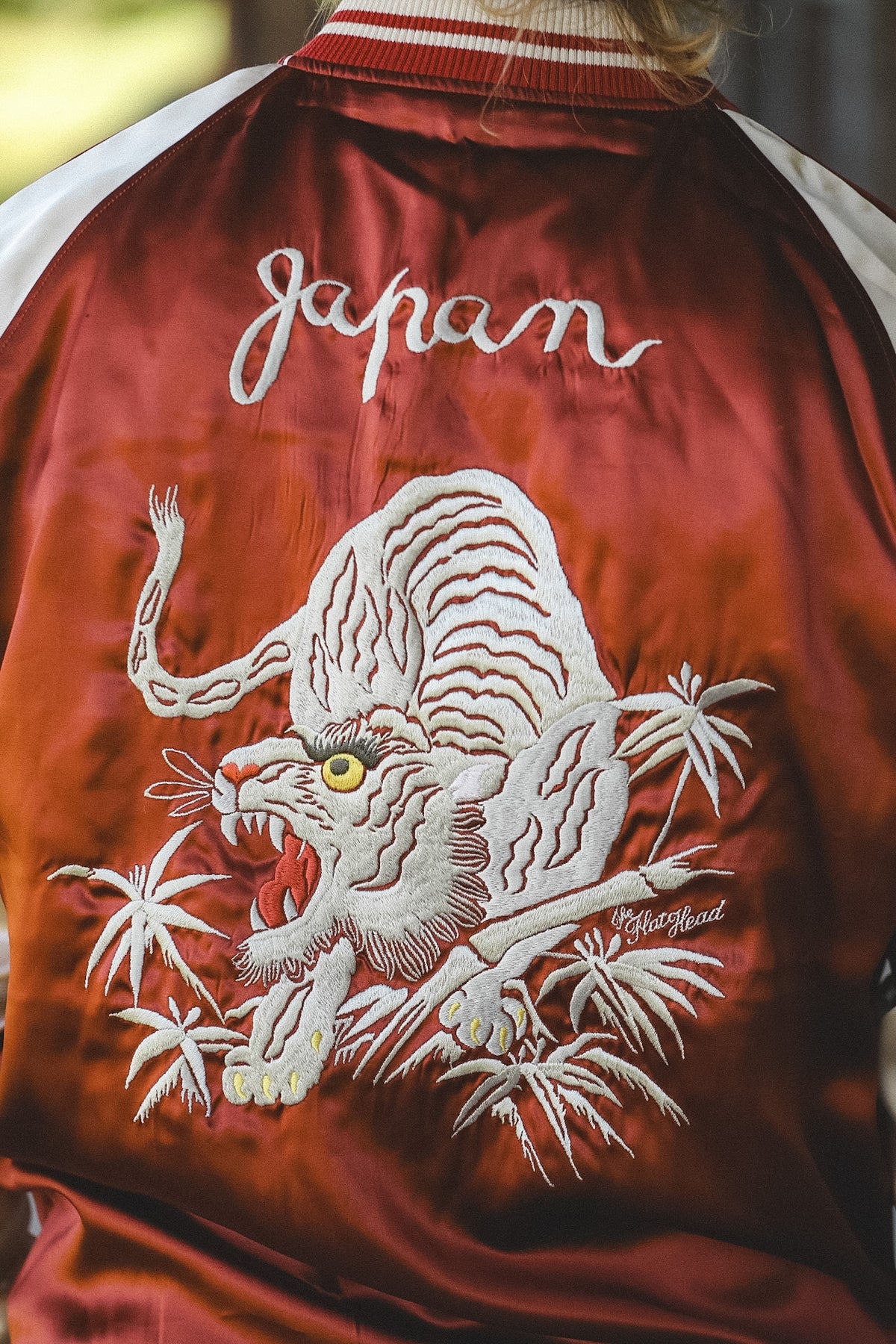 Close-up of the back of a satin bomber jacket in deep red, featuring a large white embroidered tiger, bamboo, and the word 'Japan' in white script.
